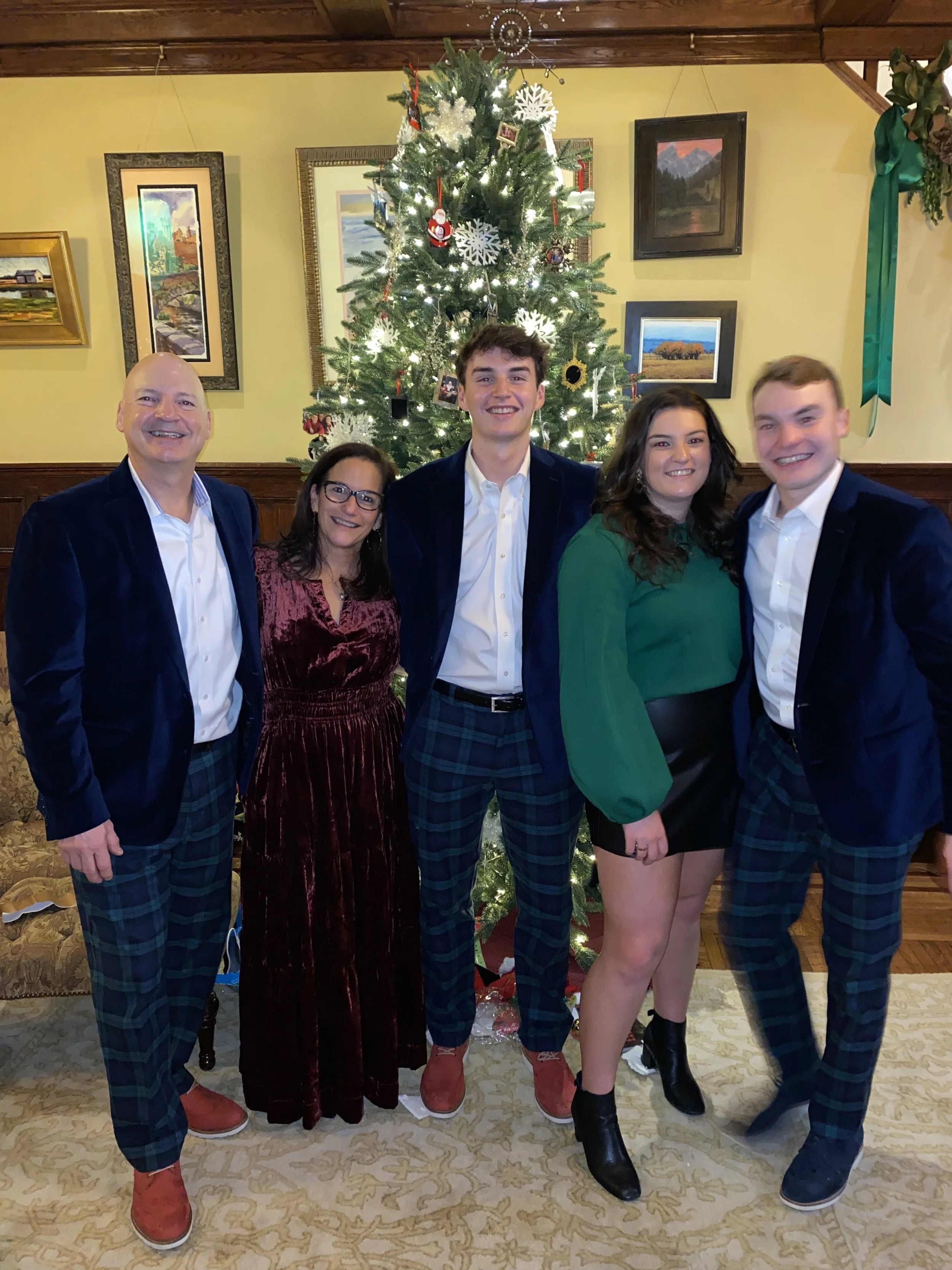 Family standing in front of a decorated Christmas tree, smiling for a group photo indoors.
