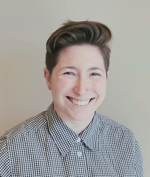 Headshot of Rachel with a warm smile, short hair and checkered button down shirt.