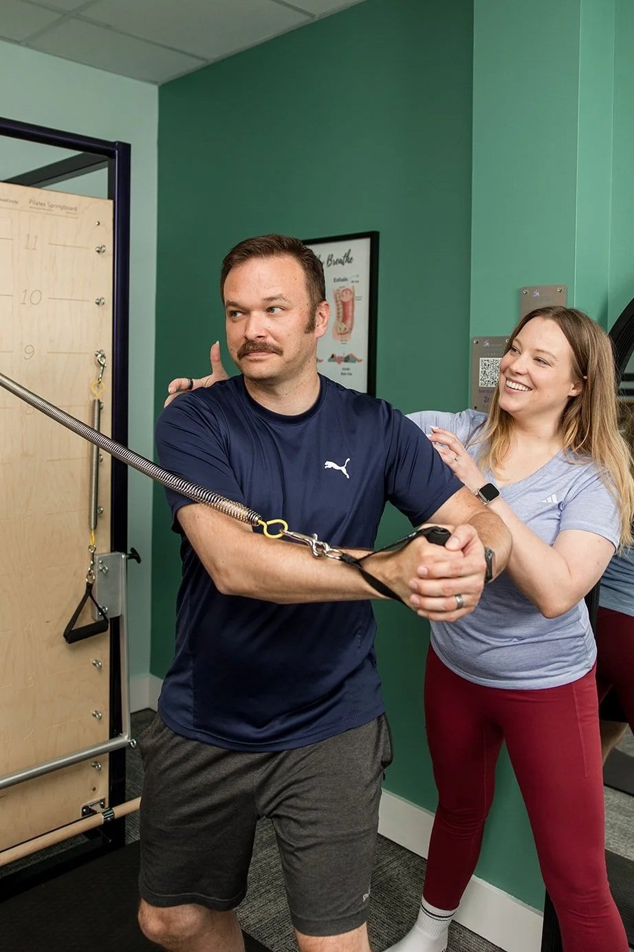 woman giving shoulder correction to man doing Pilates on the tower