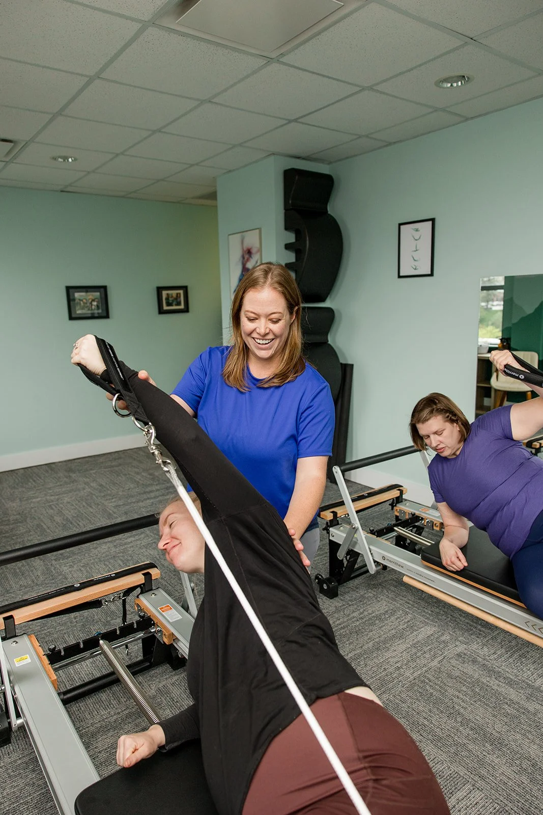 pilates instructor teaching a side lying overhead press on the reformer to a semiprivate session