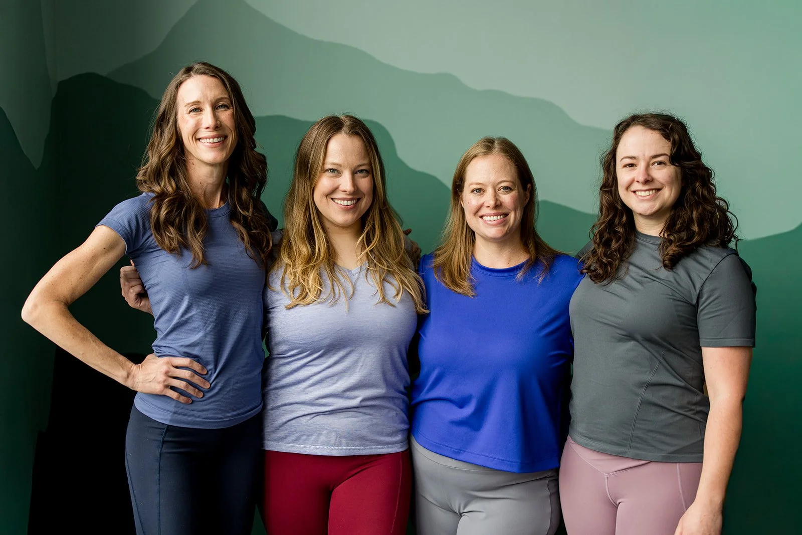 Four women in athletic clothes posing in front of a mountain mural