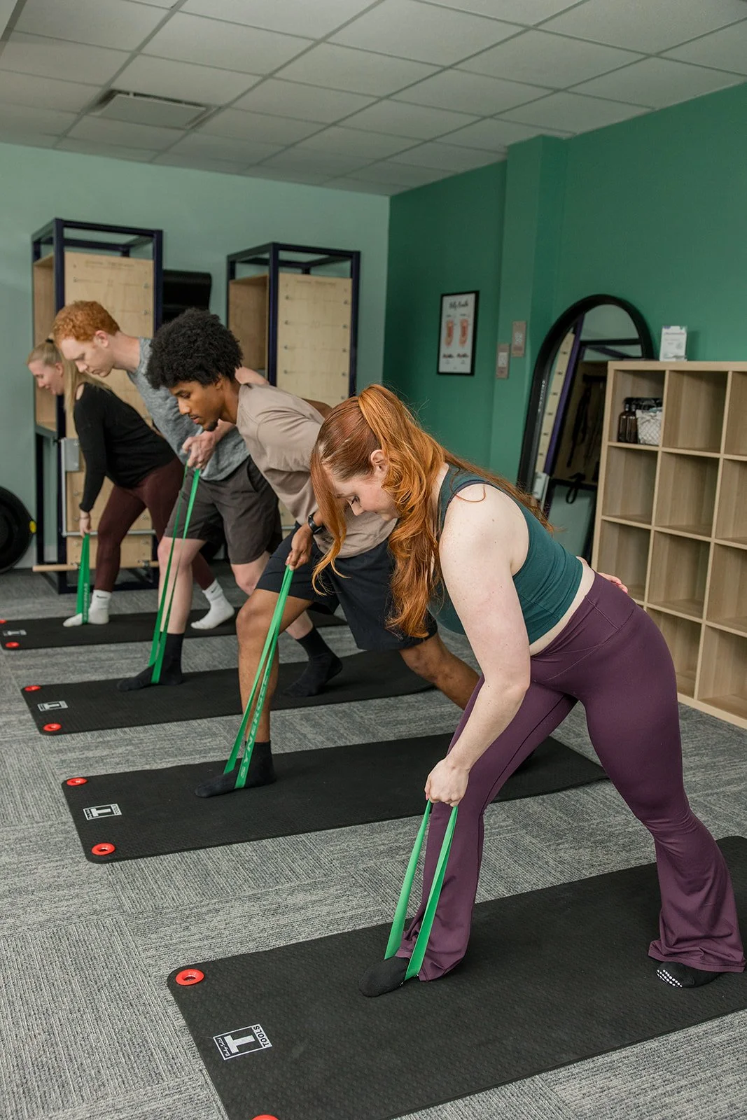 Group of four people in an exercise class, hinged forward rowing with a resistance band