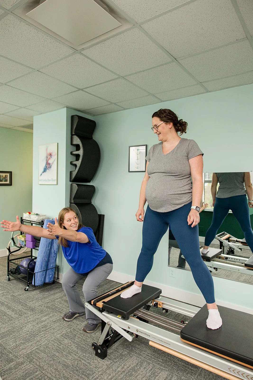 Pilates instructor demonstrating squat to a pregnant woman on the reformer