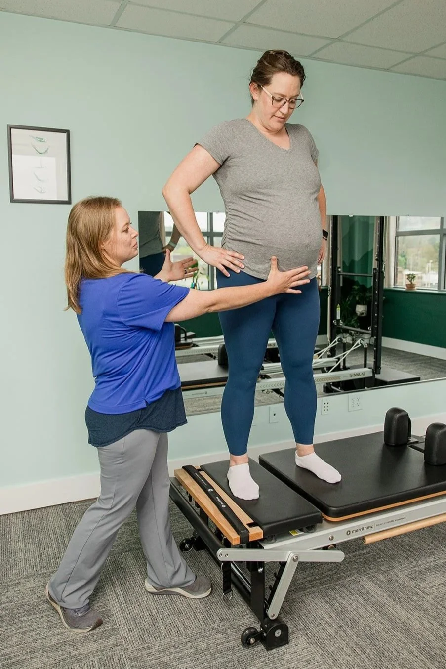 woman giving feedback to pregnant mom doing side splits on the reformer