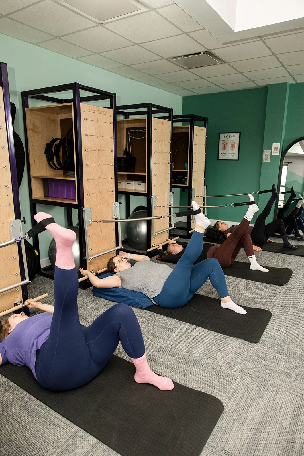 four women lying on their backs doing leg exercises on the Pilates springboard tower