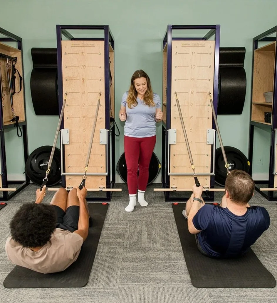 woman teaching two men a rolldown on the pilates springboard
