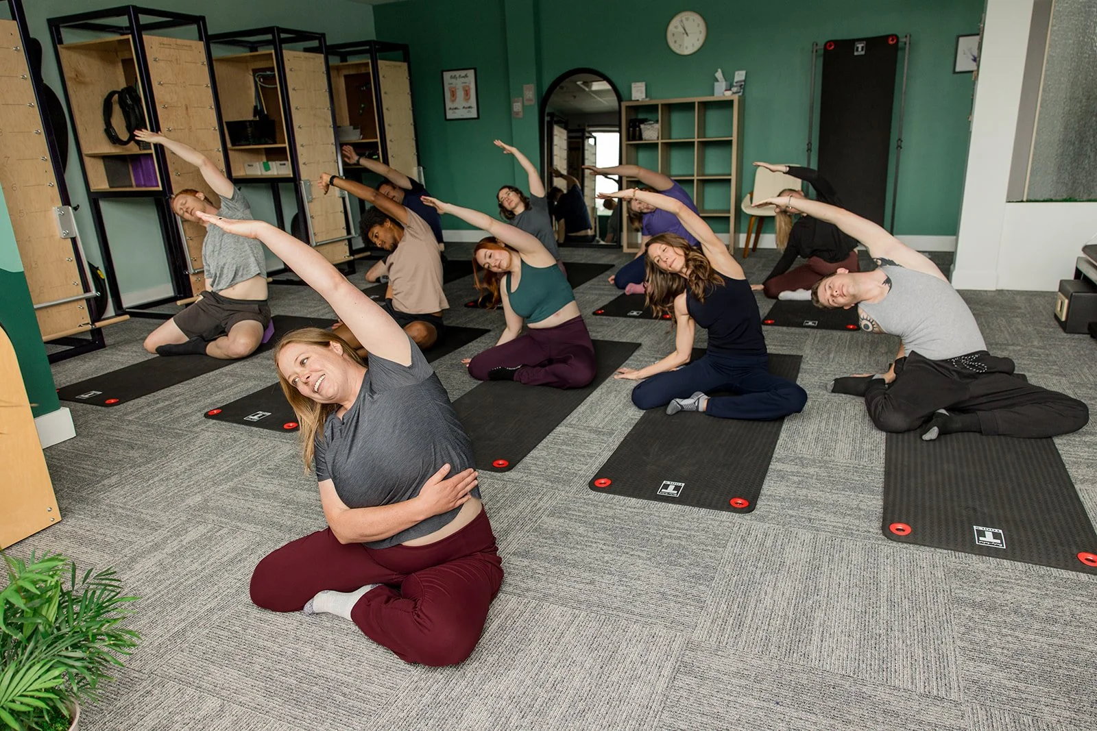 A group of men and women in a group pilates mat class performing a sidebend mermaid stretch