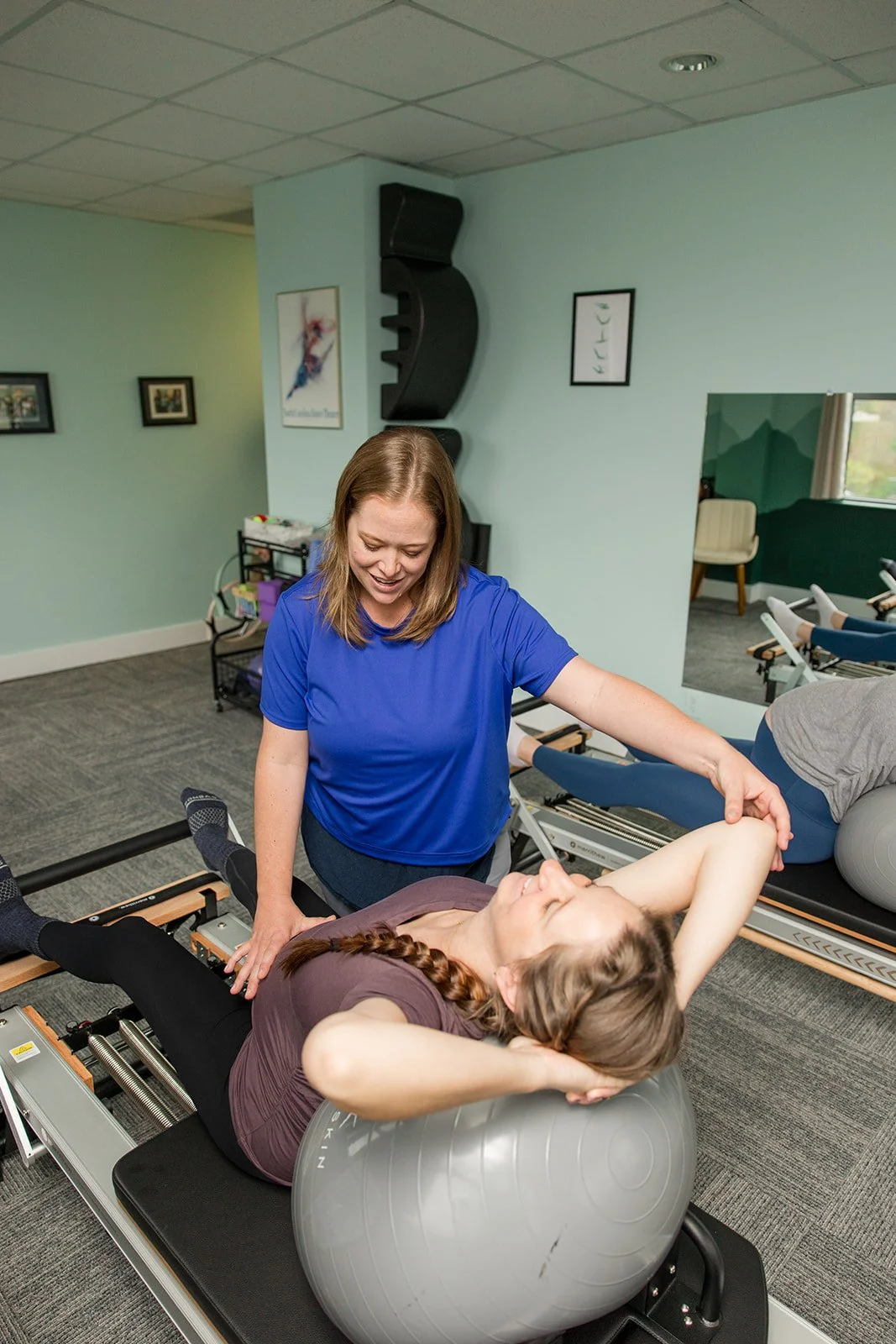 pilates instructor providing gentle corrections to prenatal mom during a pilates session on the reformer