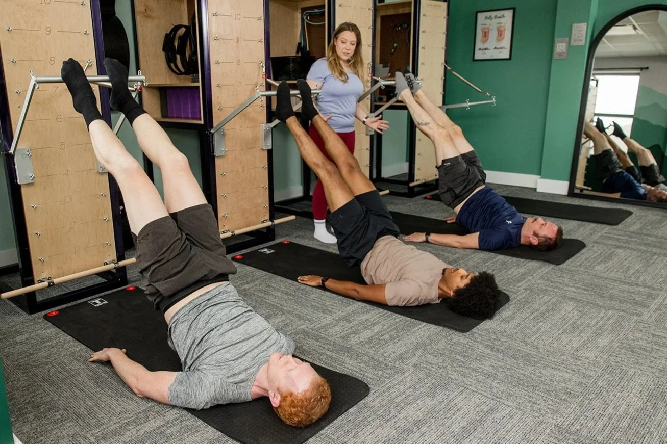 woman teaching three men parakeet exercise on the pilates tower