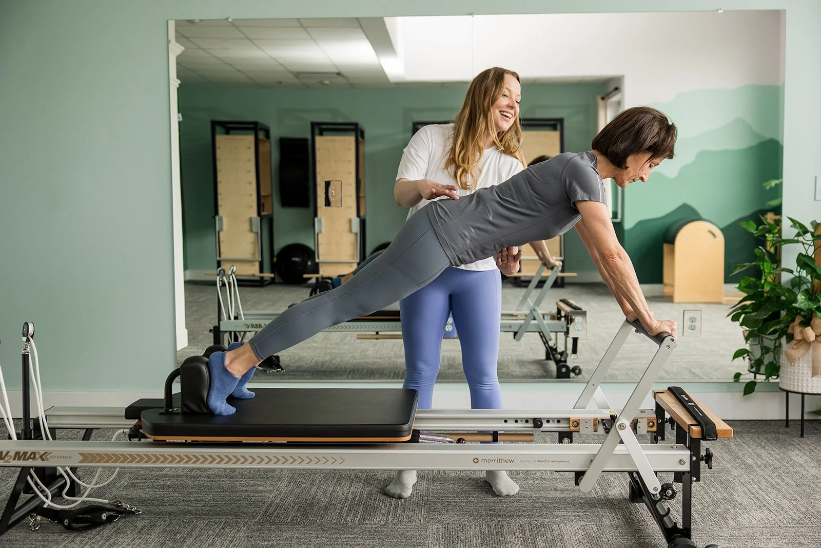 Smiling instructor teaching a plank exercise on the Pilates reformer