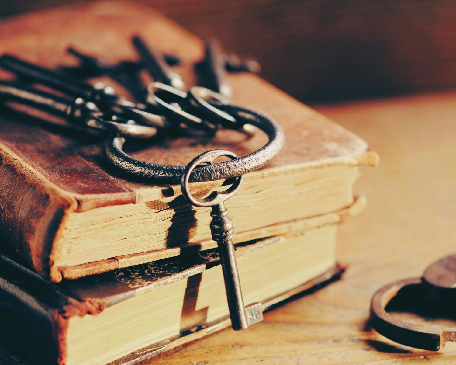 An old, weathered book with a brass lock resting on a wooden surface. A rusty, vintage key is hanging from the lock, and a leather strap is nearby. The scene is warm and nostalgic.