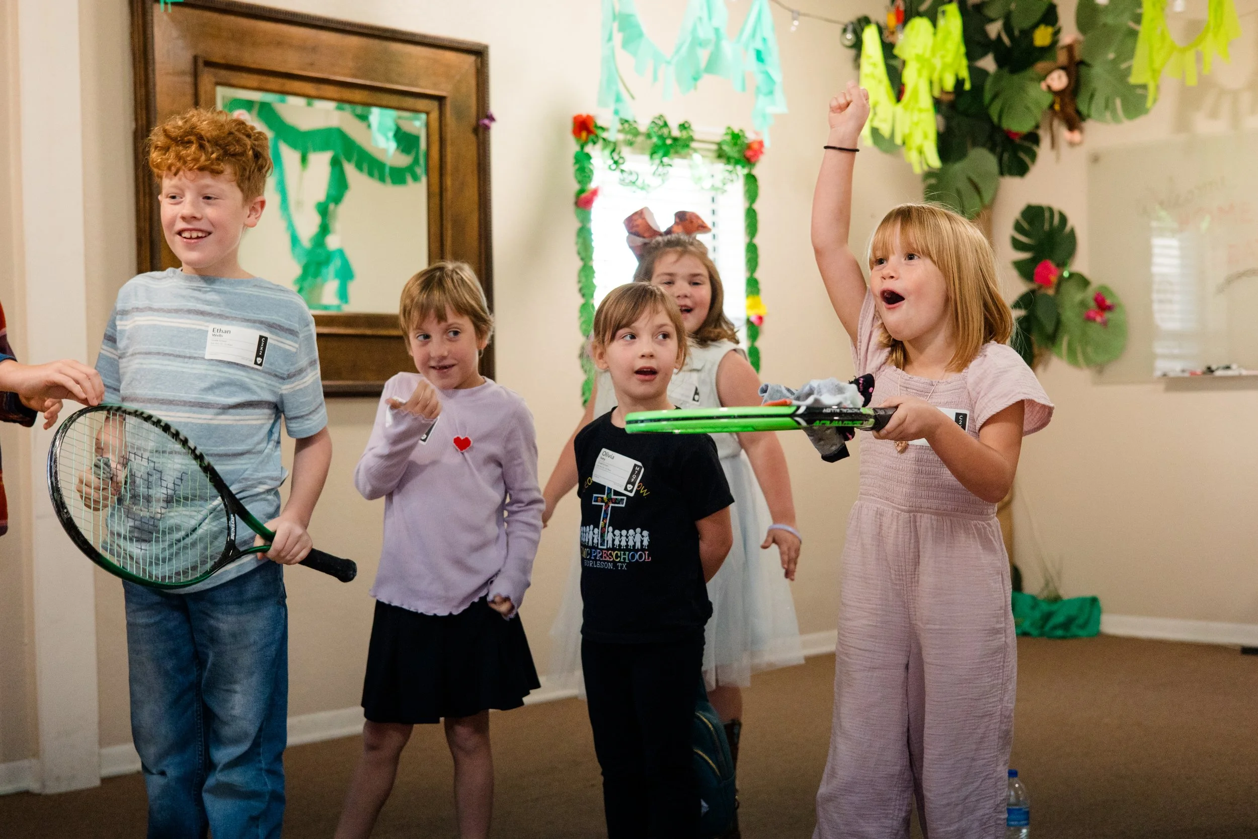 Children at a birthday party engaging in a game or activity indoors, with colorful decorations on the walls.