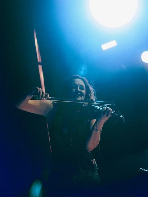 A woman playing the violin on stage under bright blue lighting.