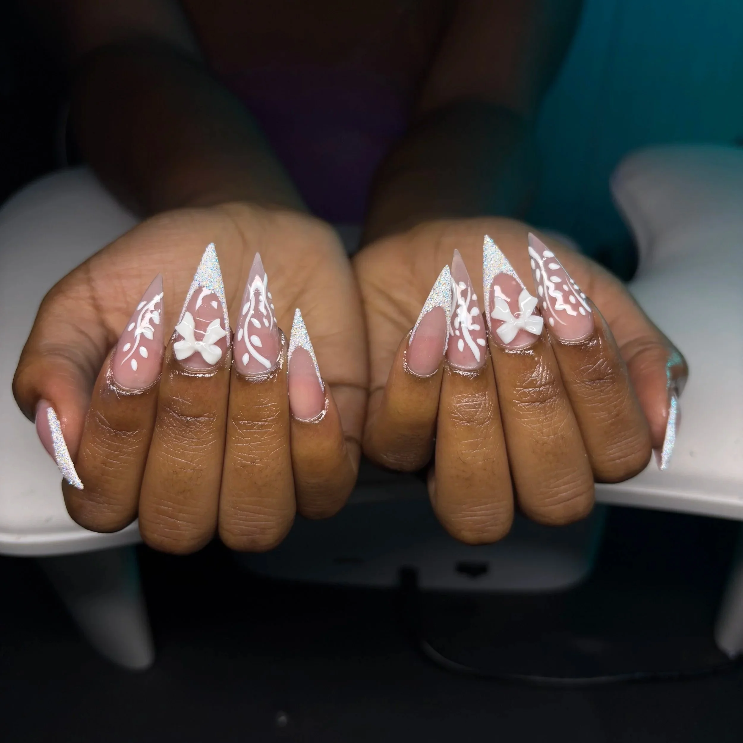 Close-up of hands with long, stiletto-shaped nails painted in pink and white with intricate designs and glitter accents.