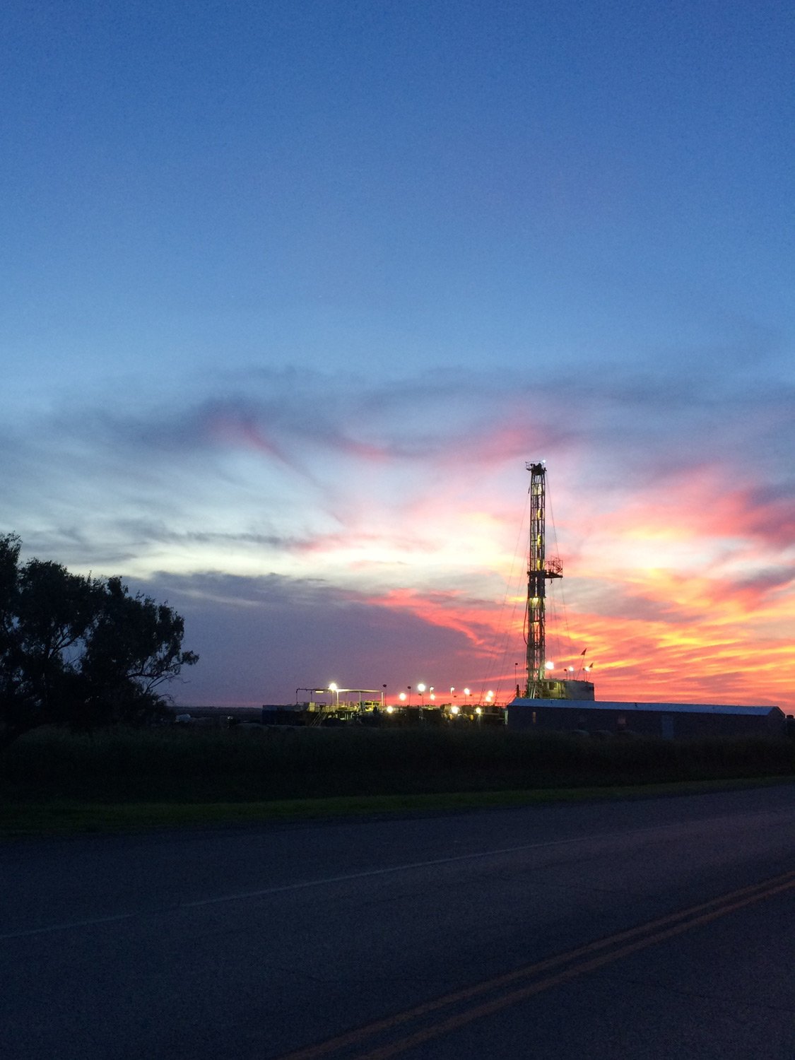 Photo of an oil drilling rig at sunset showing active mid continent gas exploration work in the field
