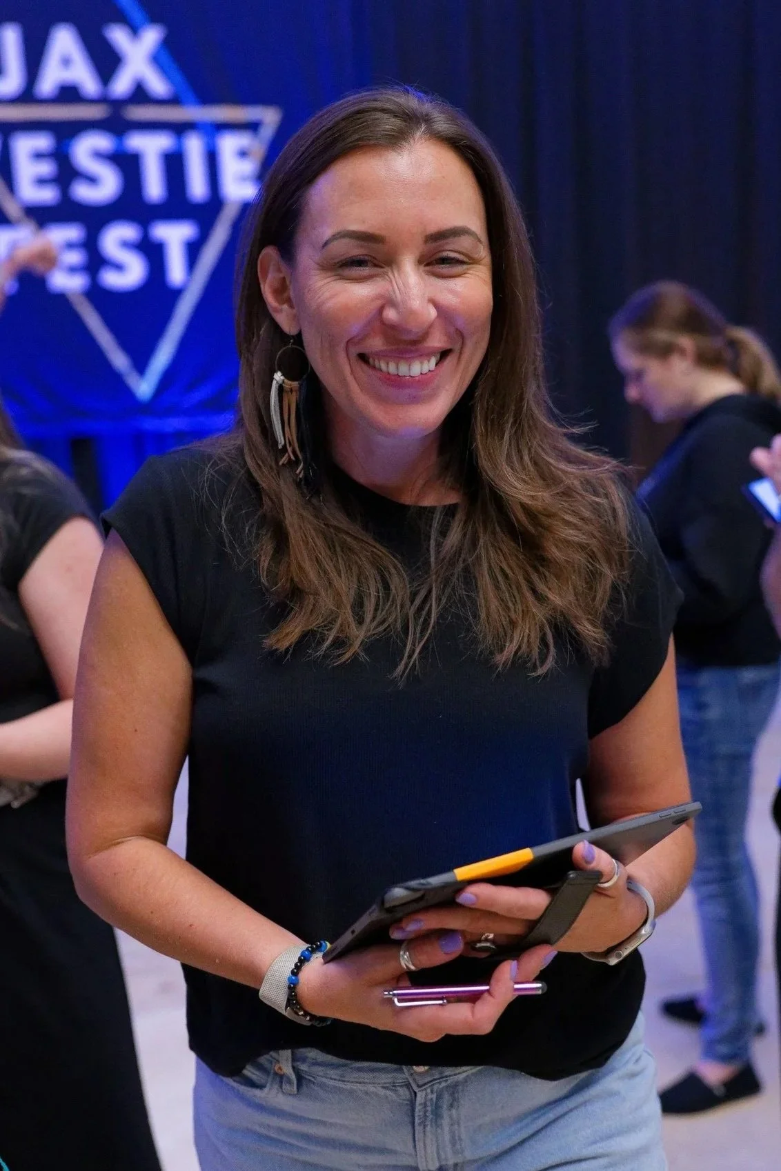 Woman smiling and holding a tablet at an event with a Ajax entertainment sign in the background.