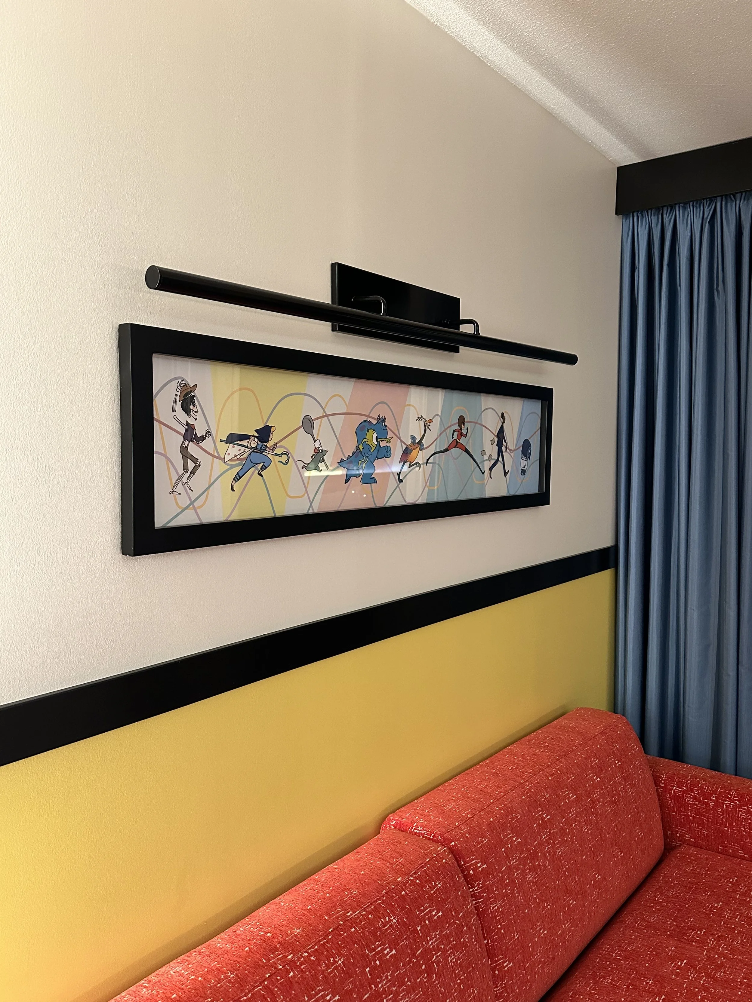 Colorful framed abstract art hanging above a yellow wall with a red sofa and blue curtains in the room.