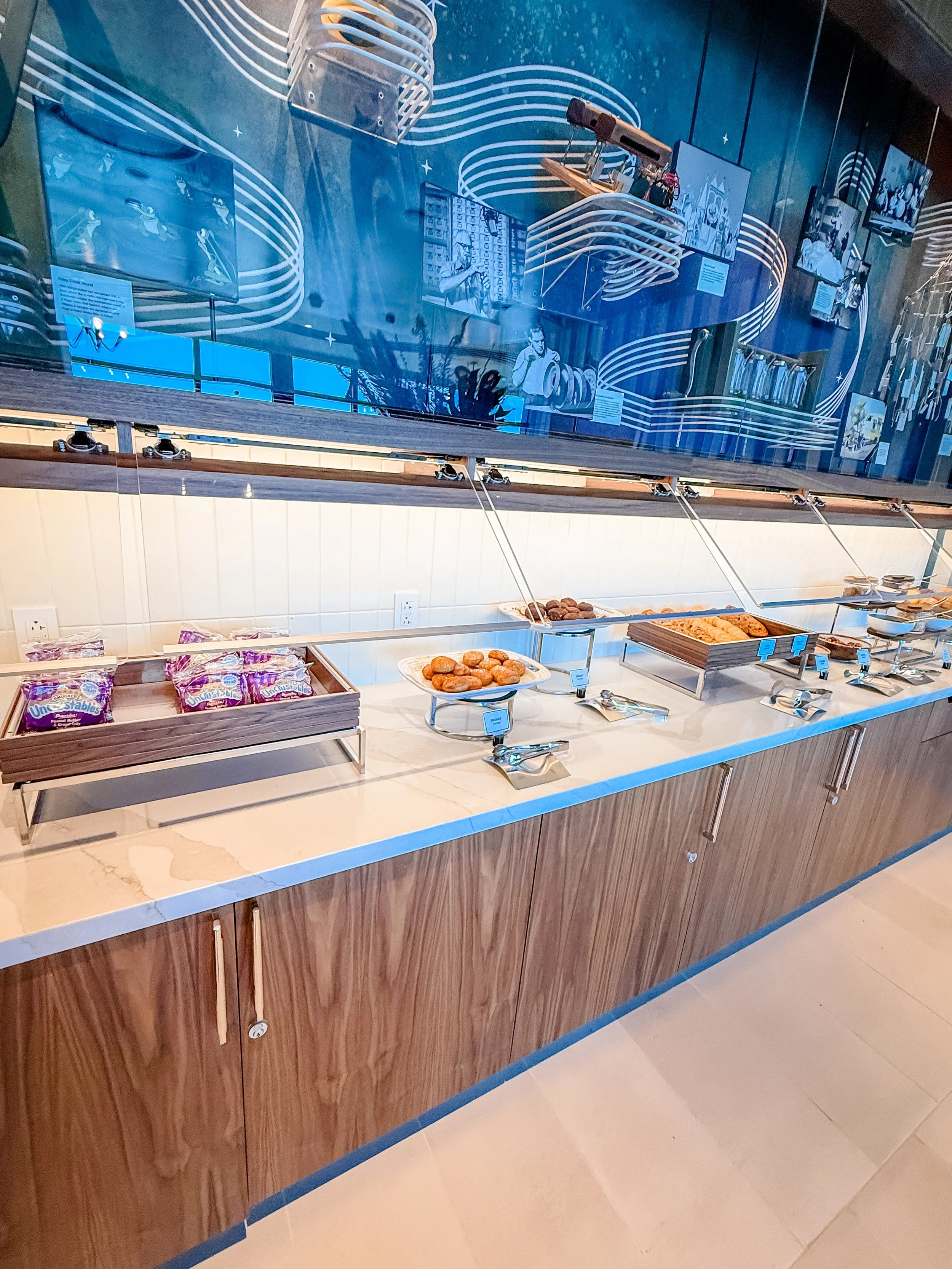 Buffet table with various pastries and snacks in a cafeteria setting with a blue abstract wall art backdrop.