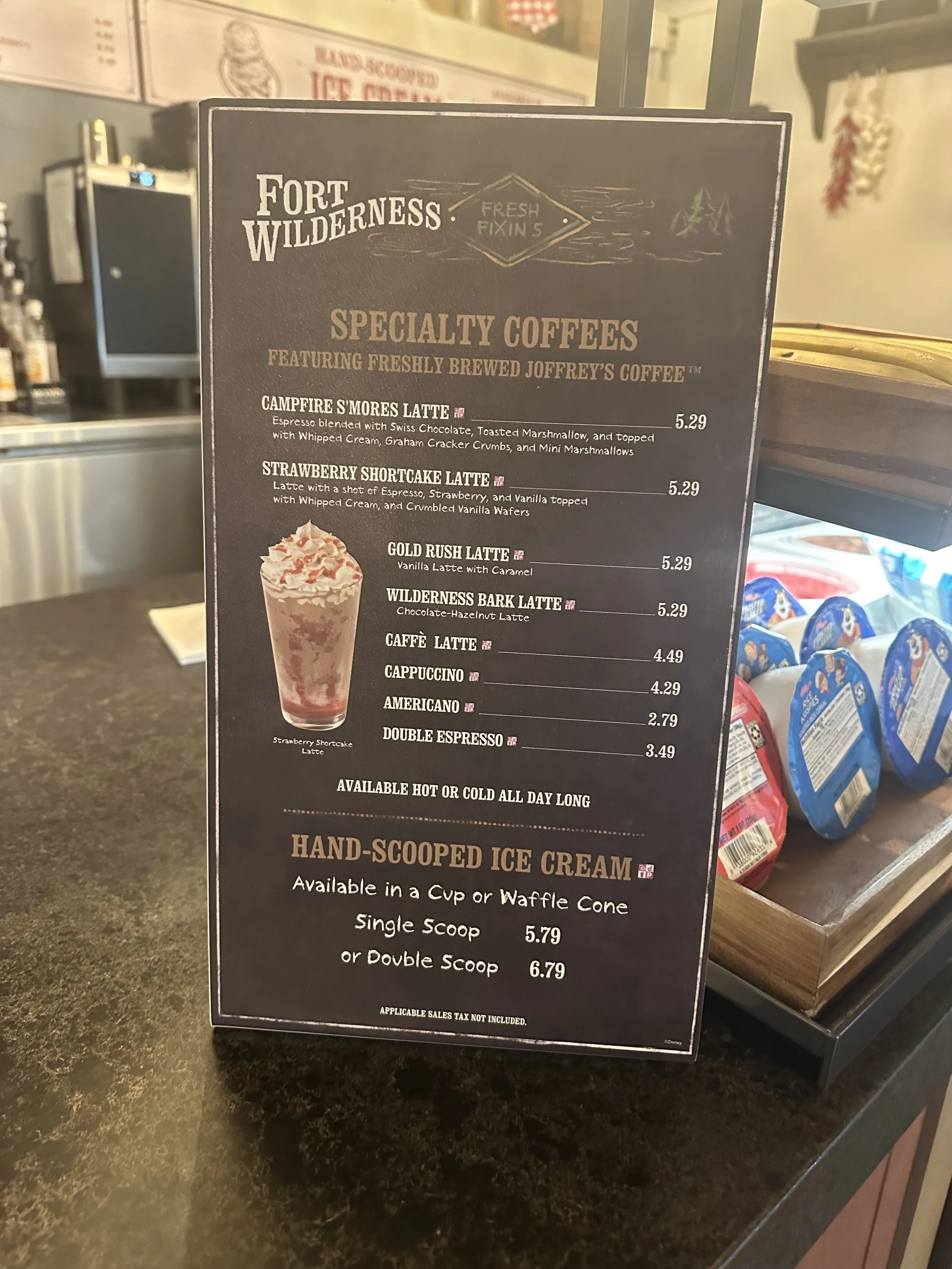 Coffee shop menu featuring specialty coffees, including Campfire S'mores Latte, Strawberry Shortcake Latte, Gold Rush Latte, Wilderness Bark Latte, and various espresso drinks, along with hand-scooped ice cream options.