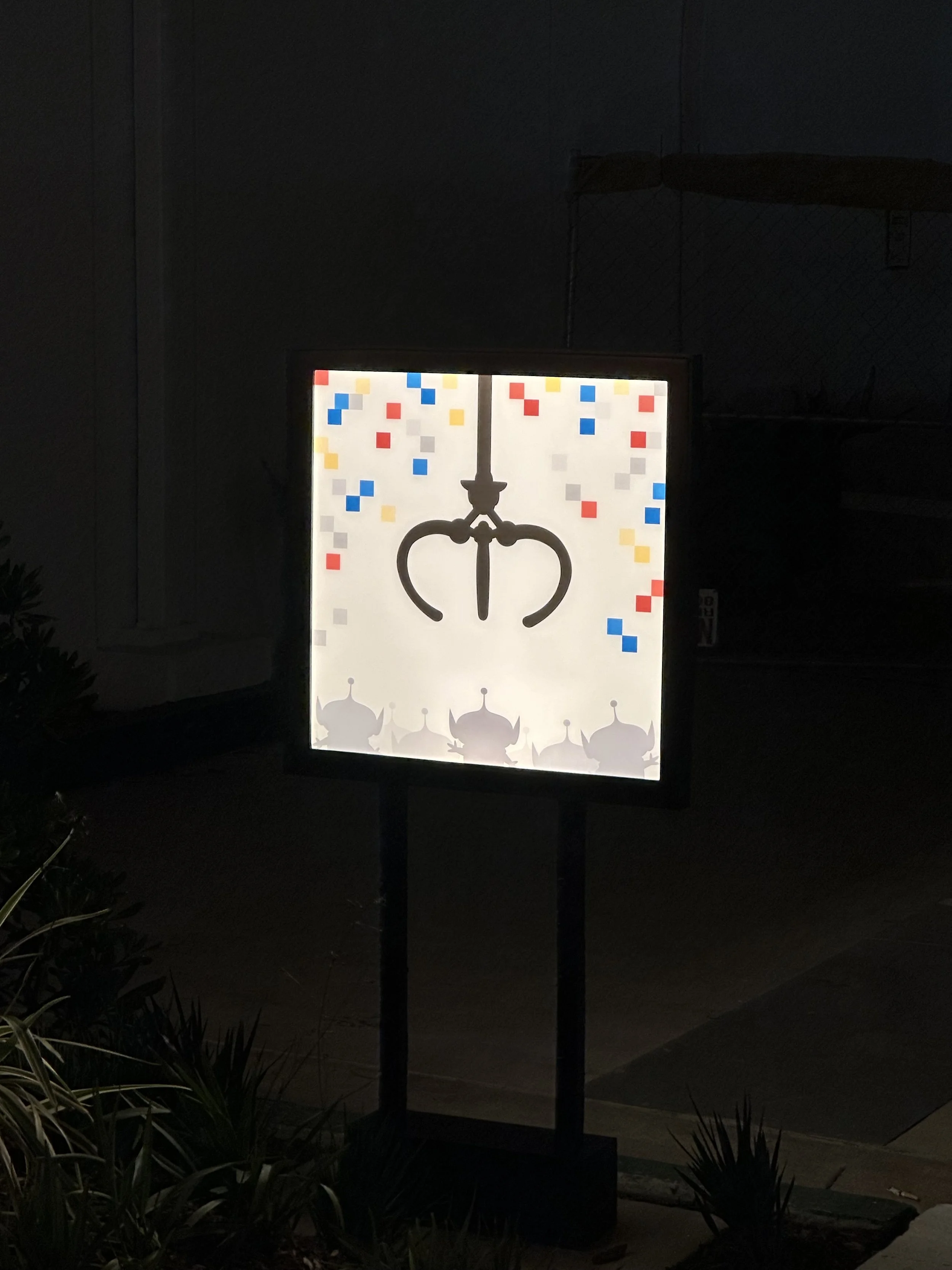 Illuminated sign with a claw machine's grabbing arm and colorful confetti background, with shadowy potato-shaped characters at the bottom.