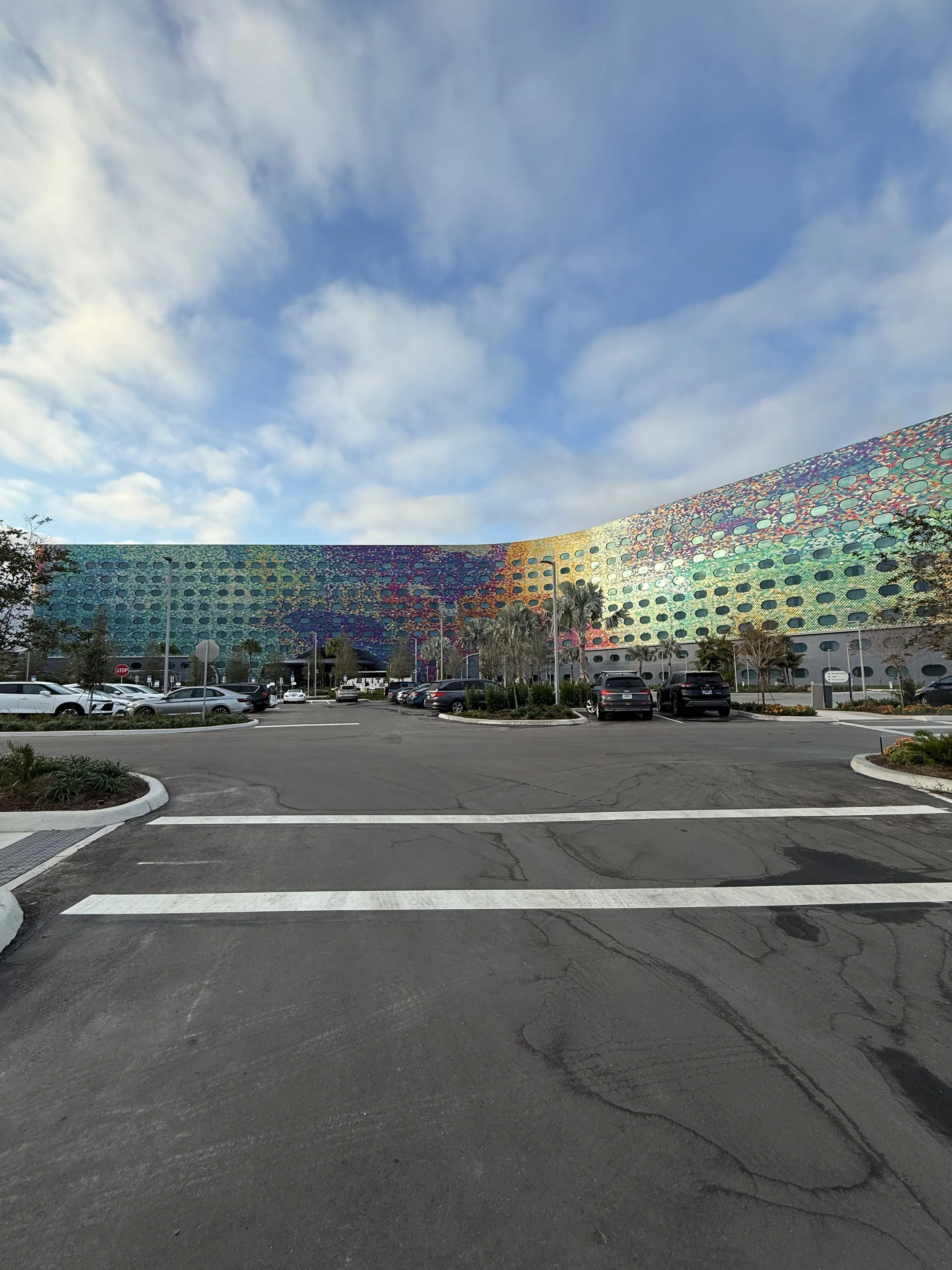 Colorful, patterned building with a parking lot and cars in front, under a partly cloudy sky.