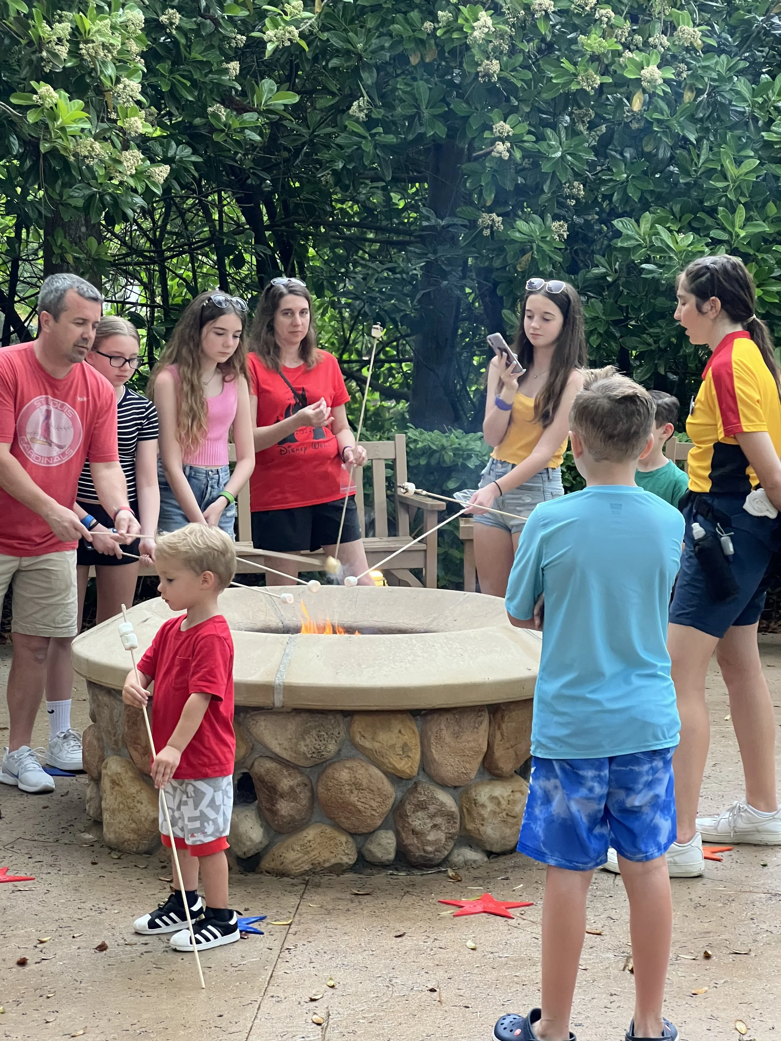 Group of children and adults around a fire pit roasting marshmallows outdoors.