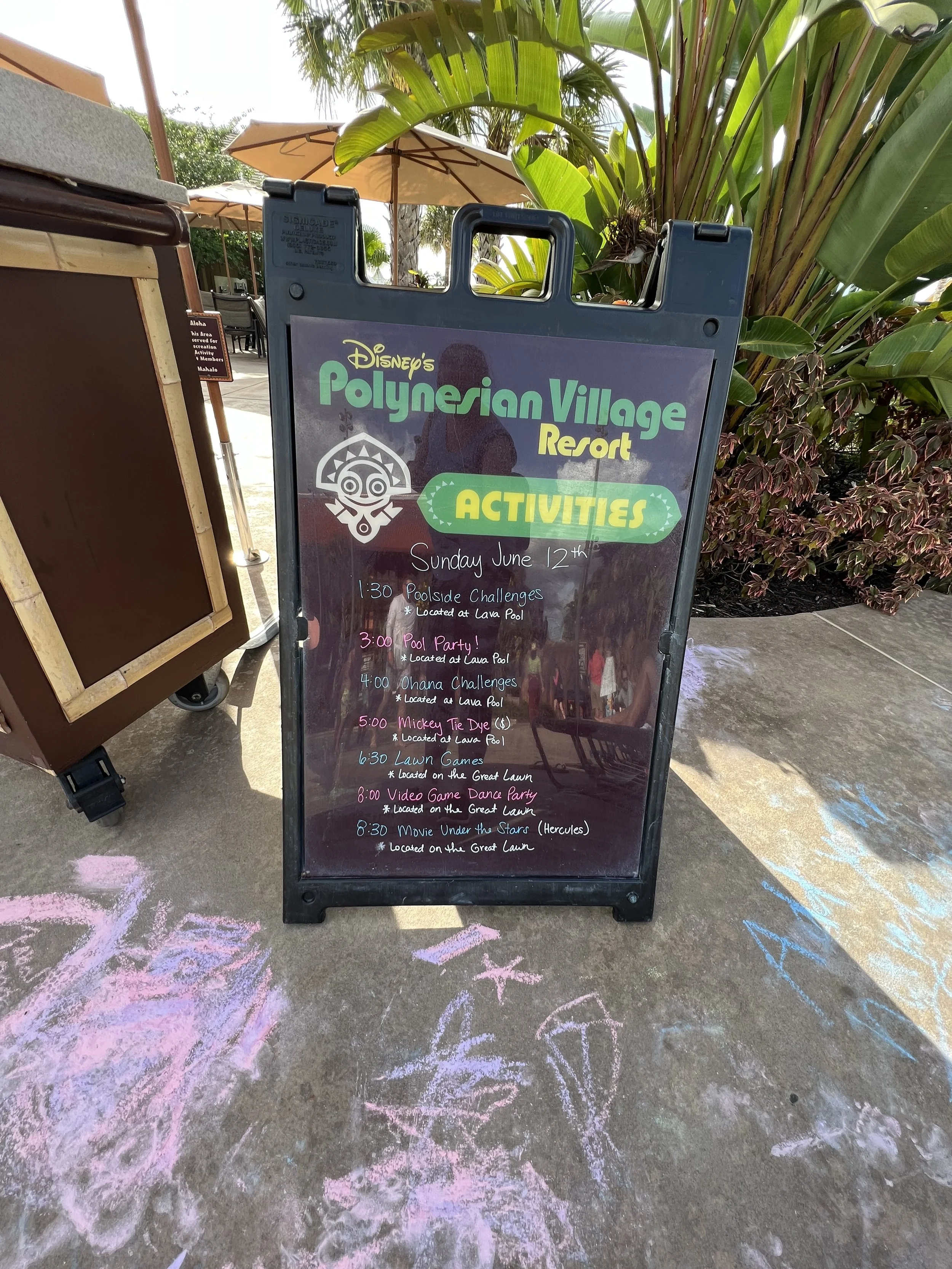 Signboard listing activities for Disney's Polynesian Village Resort on June 12th, including poolside challenges, pool party, ohana challenges, lawn games, video game dance party, and movie night, with some activities located at Lava Pool and the Grea