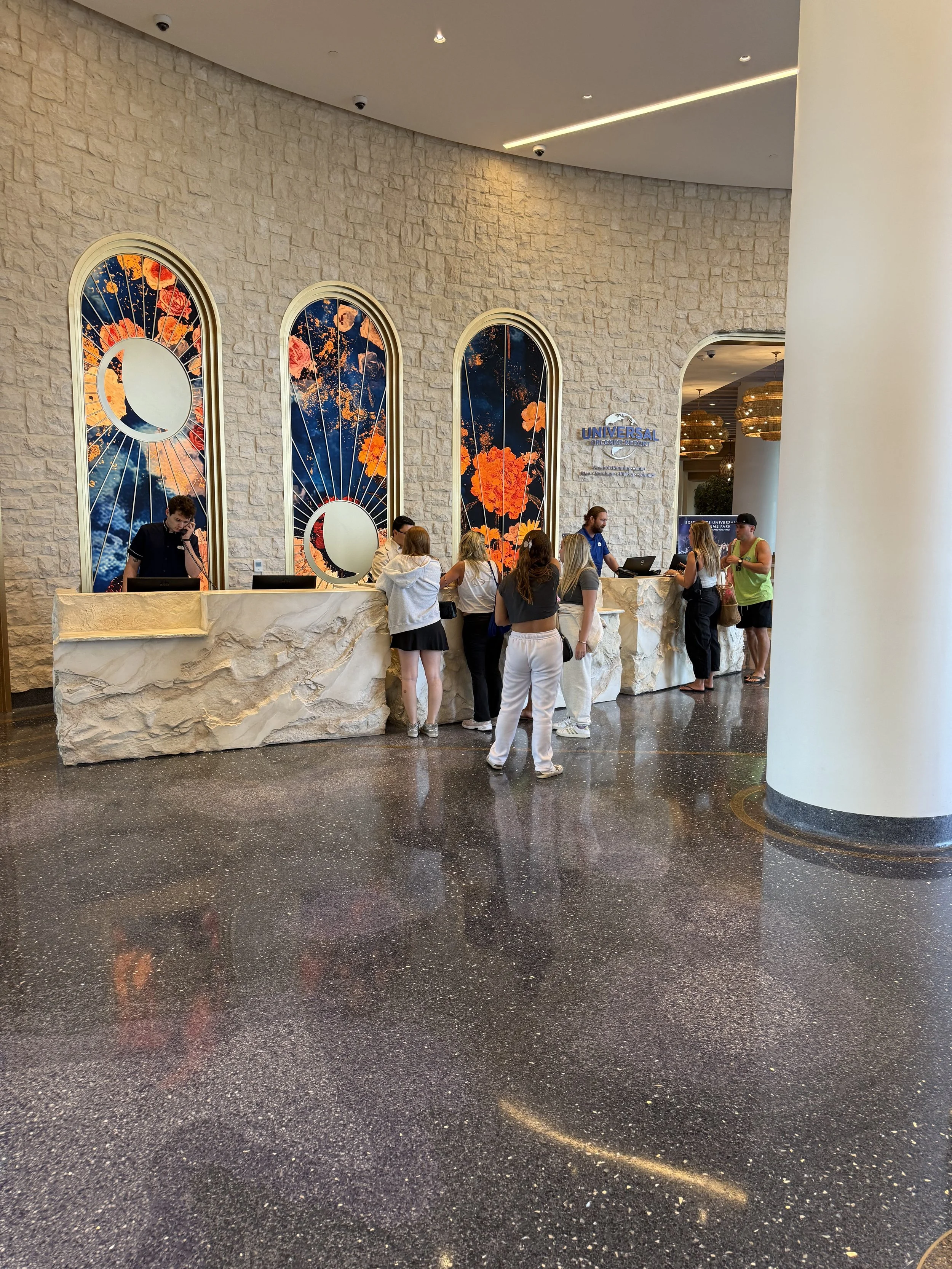 People standing at a hotel reception desk inside a building with a stone wall and colorful stained glass windows in the background.