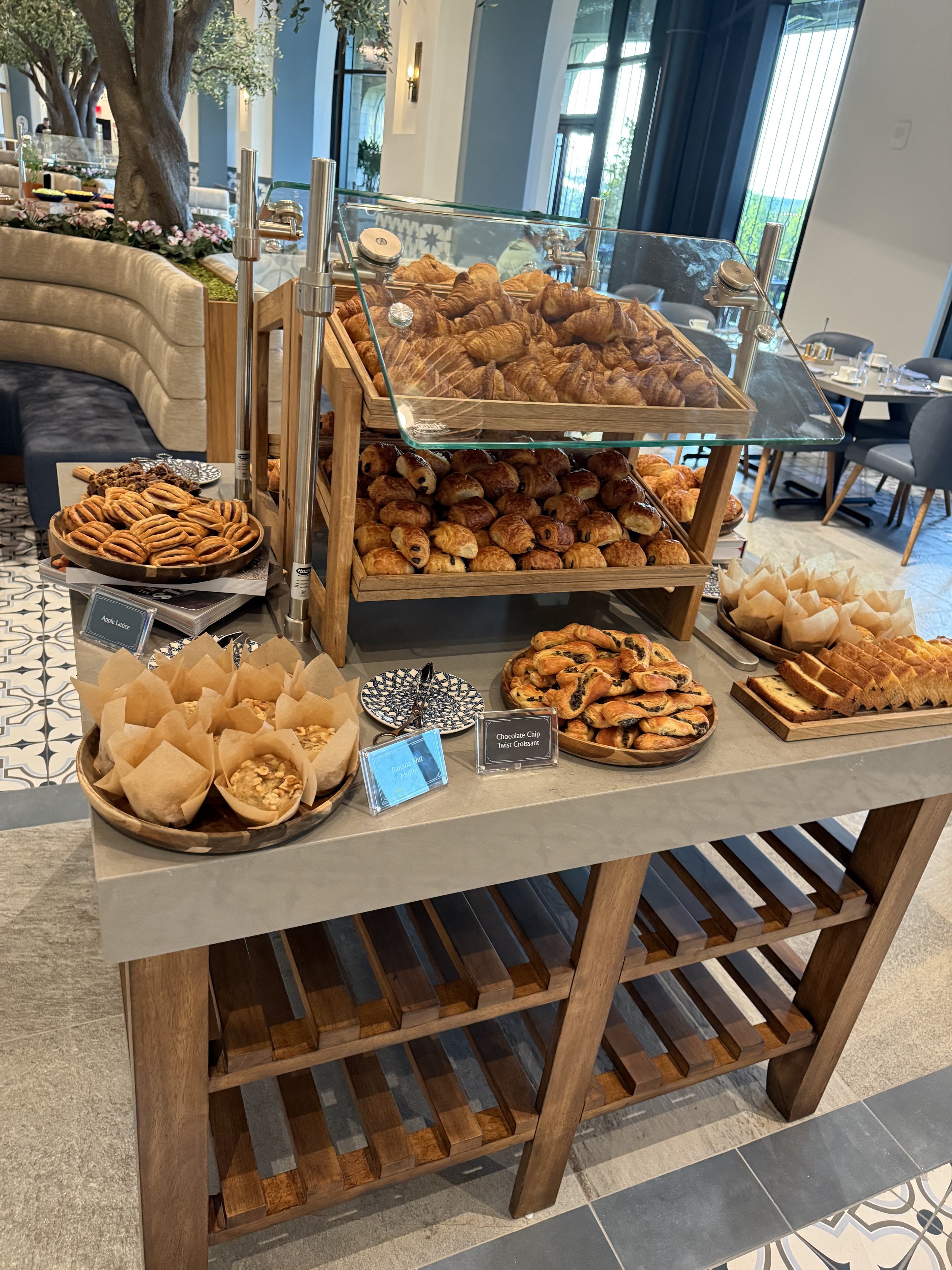 Bakery display with croissants, scones, cookies, and muffins in a hotel or café setting.