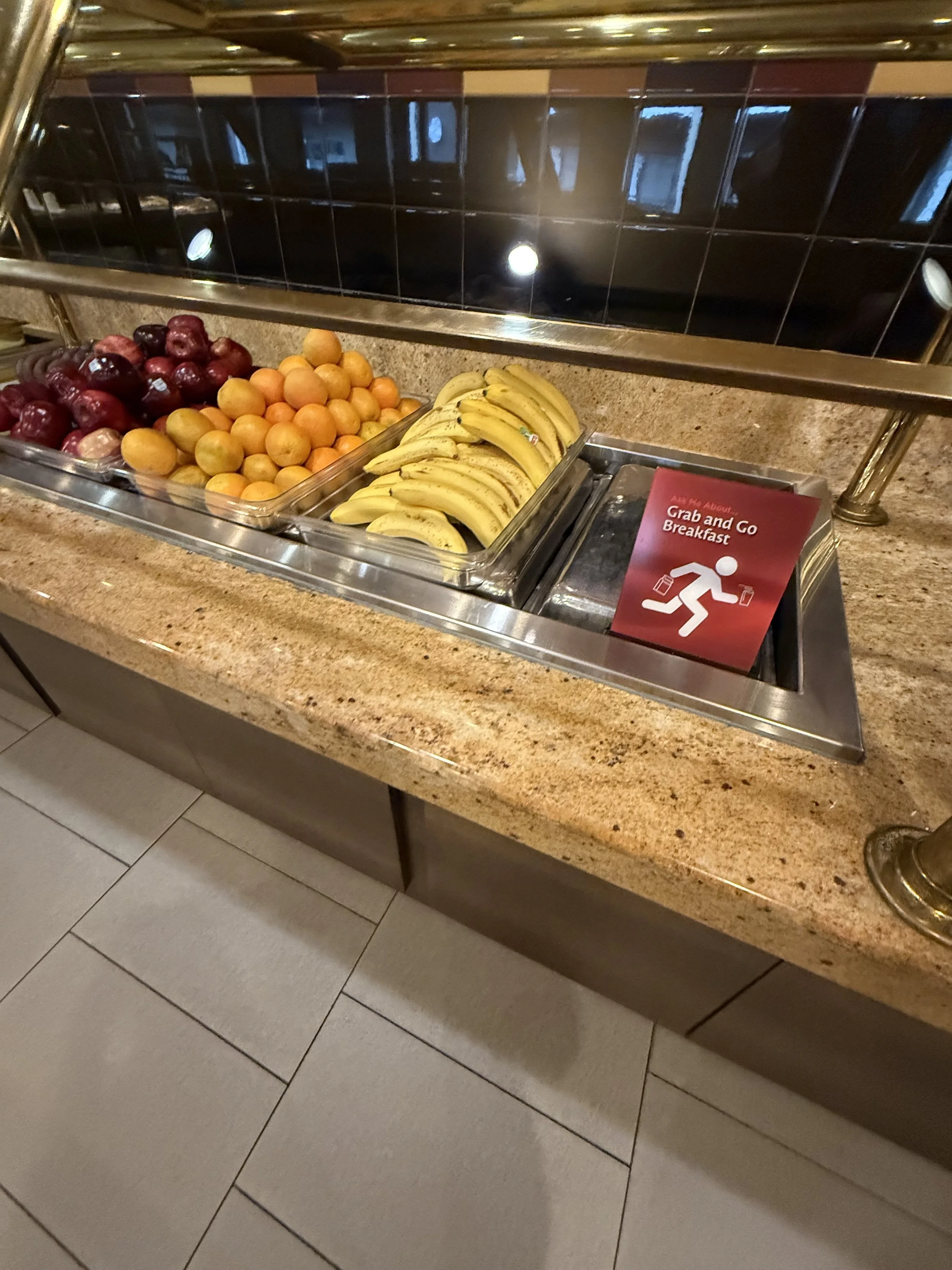 Fruits including red apples, peaches, and bananas in a buffet with a sign that reads 'Grab and Go Breakfast'.