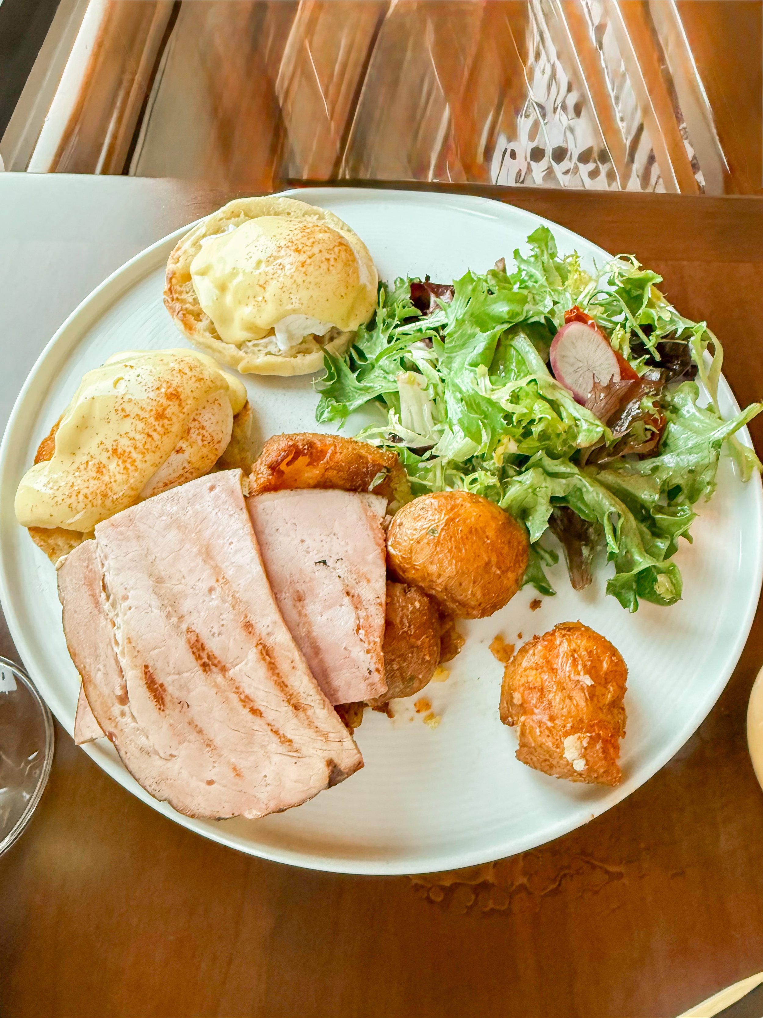 Overview of a large white plate with two eggs Benedict, sliced turkey, fried chicken and meatballs, and a side salad with lettuce and radish slices.