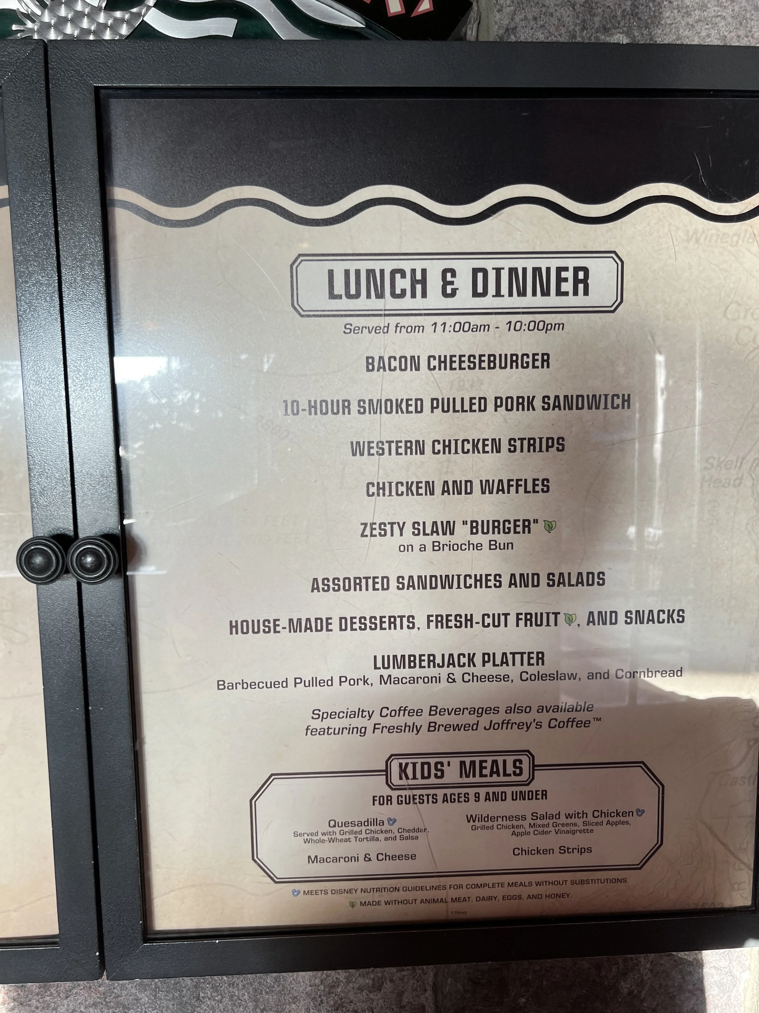 Restaurant menu board listing lunch and dinner options including bacon cheeseburger, smoked pulled pork sandwich, western chicken strips, chicken and waffles, zesty slaw burger, assorted sandwiches and salads, desserts, fruit, snacks, and lumberjack 