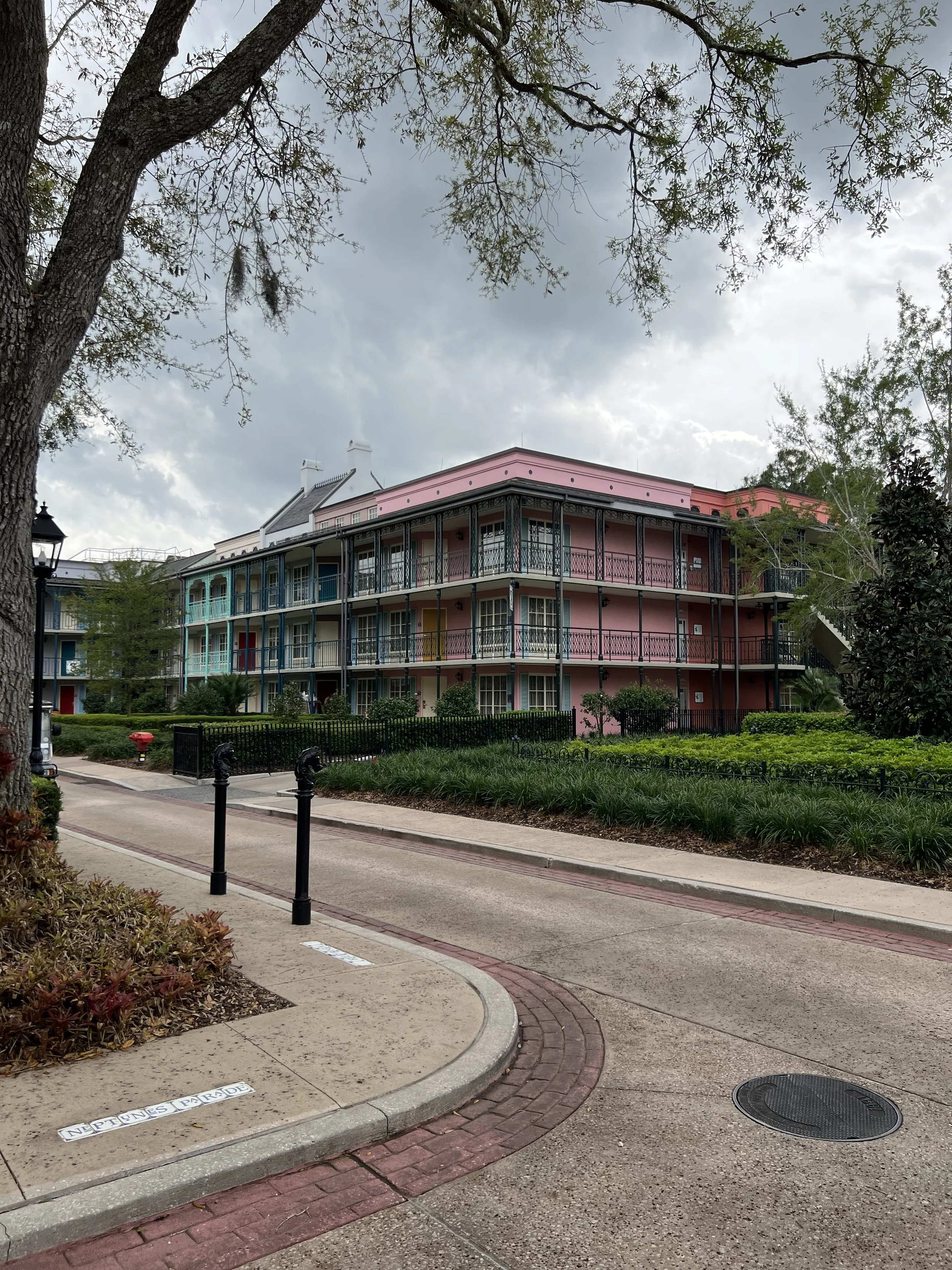 Colorful multi-story apartment building with balconies, surrounded by train tracks, greenery, and cloudy sky.