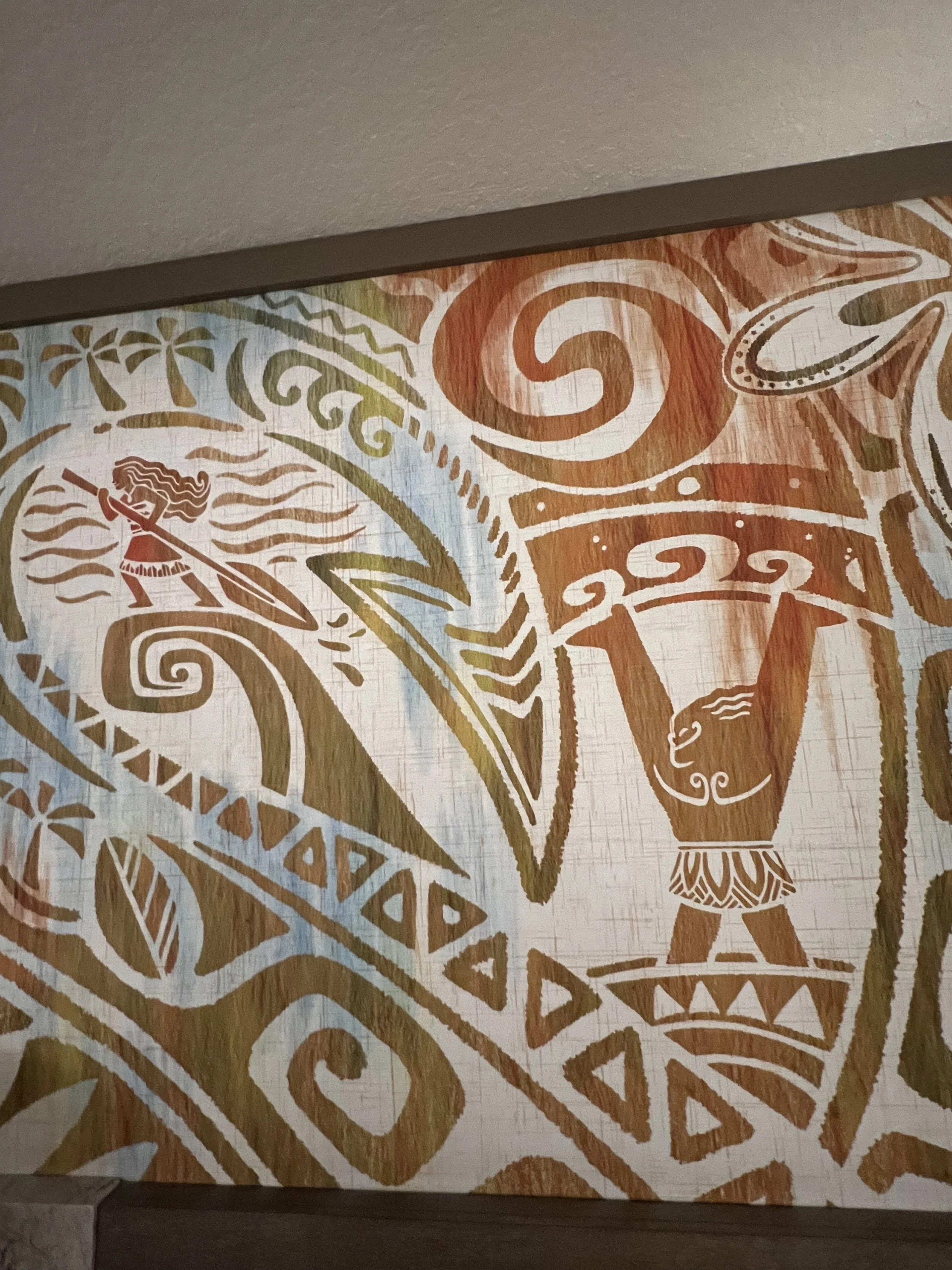 Close-up of a wall mural with Polynesian-style patterns, a person paddleboarding, and a lion.