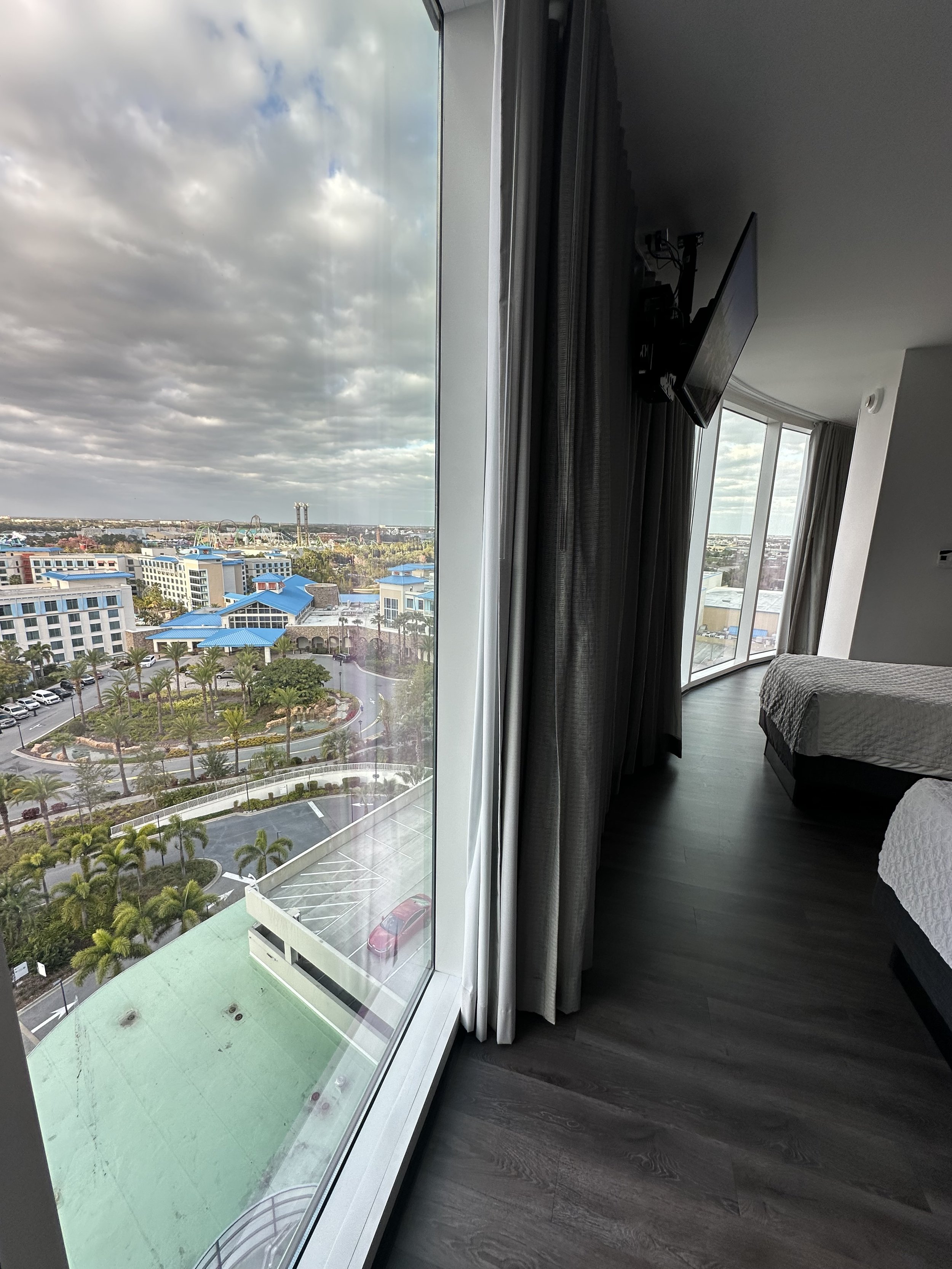 View from a hotel room window showing buildings, parking lot, palm trees, and a cloudy sky.