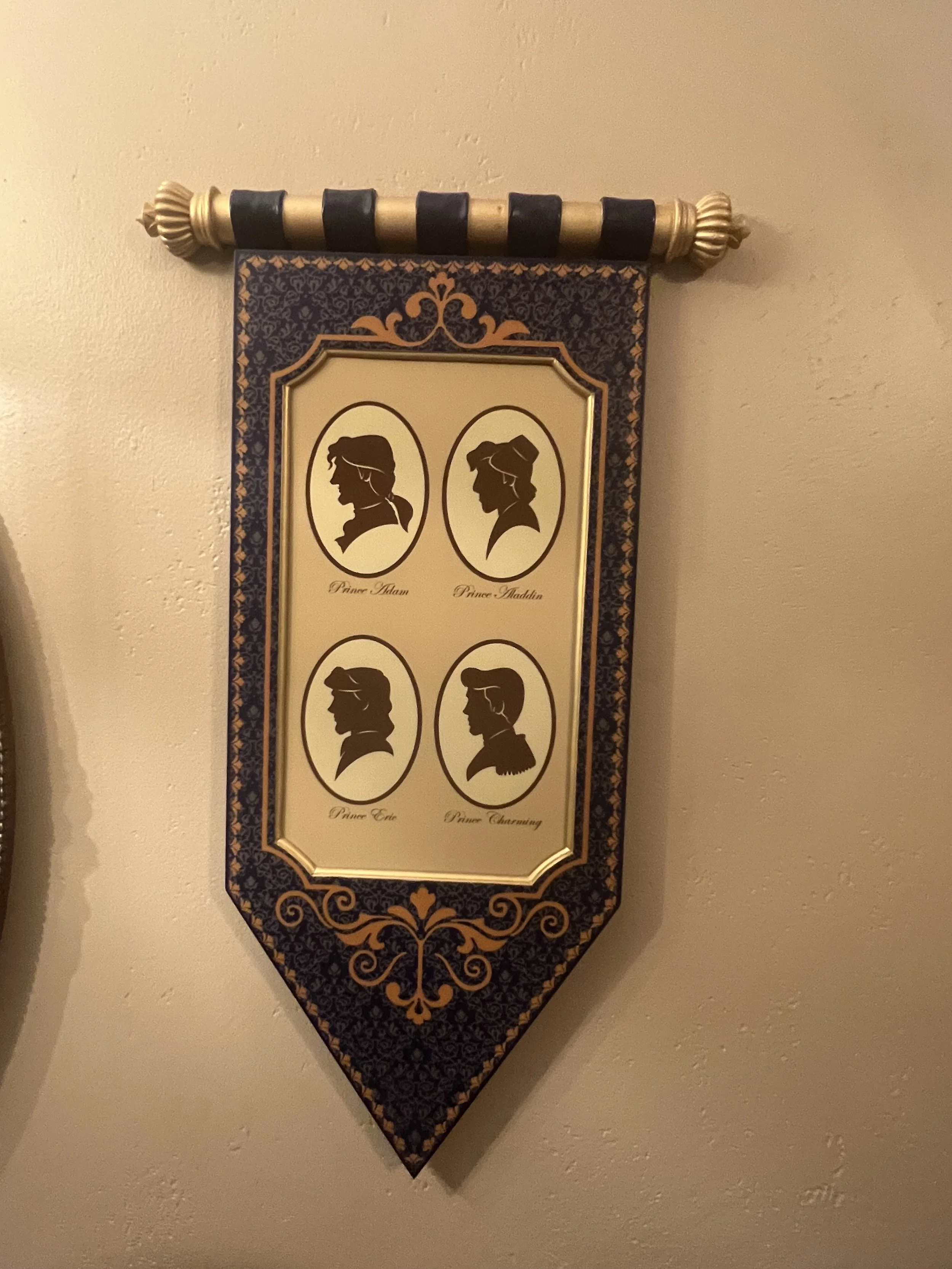 Decorative wall hanging featuring side profiles of four characters with names: Prince Adam, Prince Aladdin, Prince Eric, and Prince Charming.