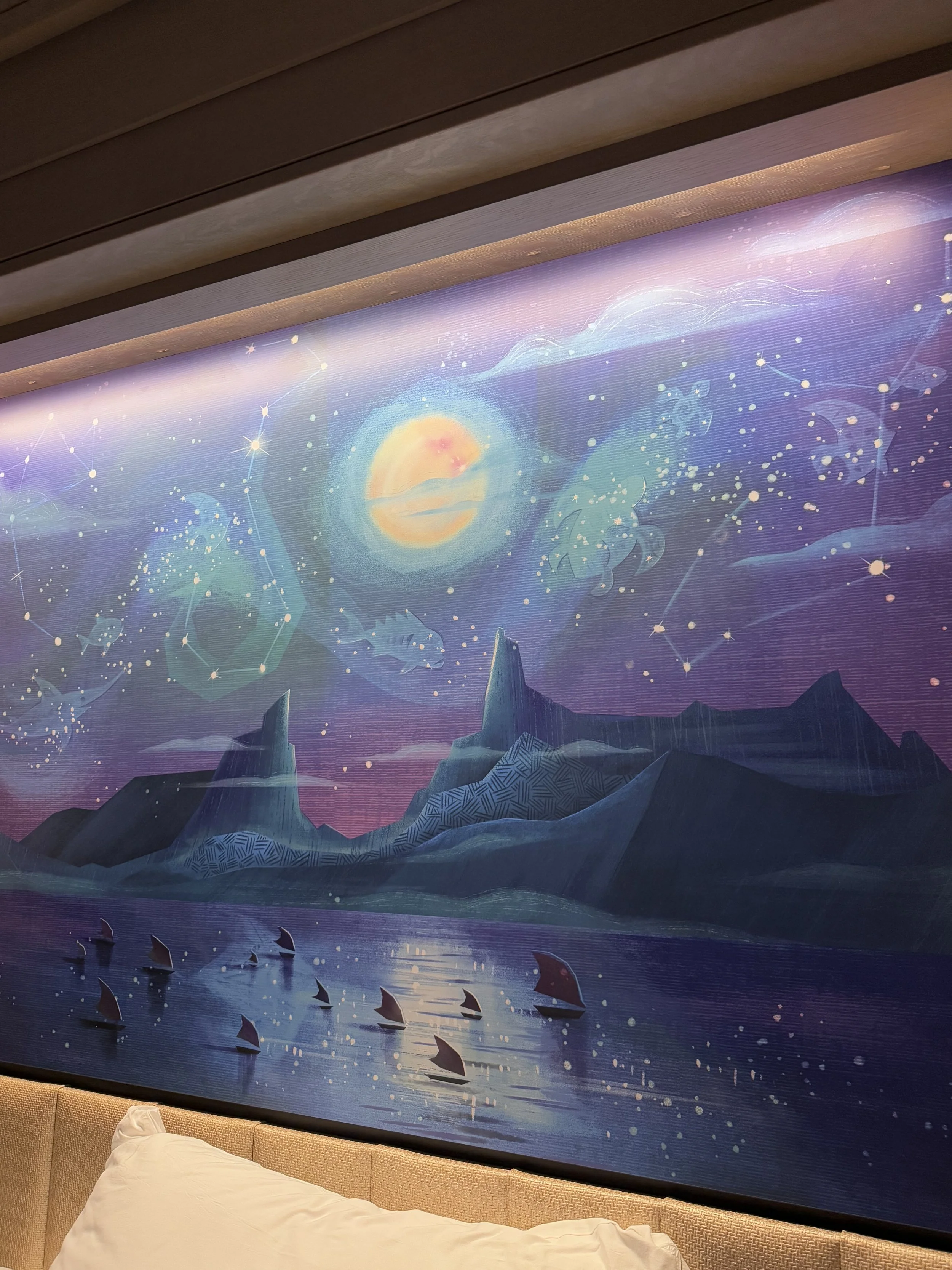 A mural depicting a mystical night sky with a glowing moon, constellations, and floating geometric shapes over icy mountains and a body of water with sailboats.