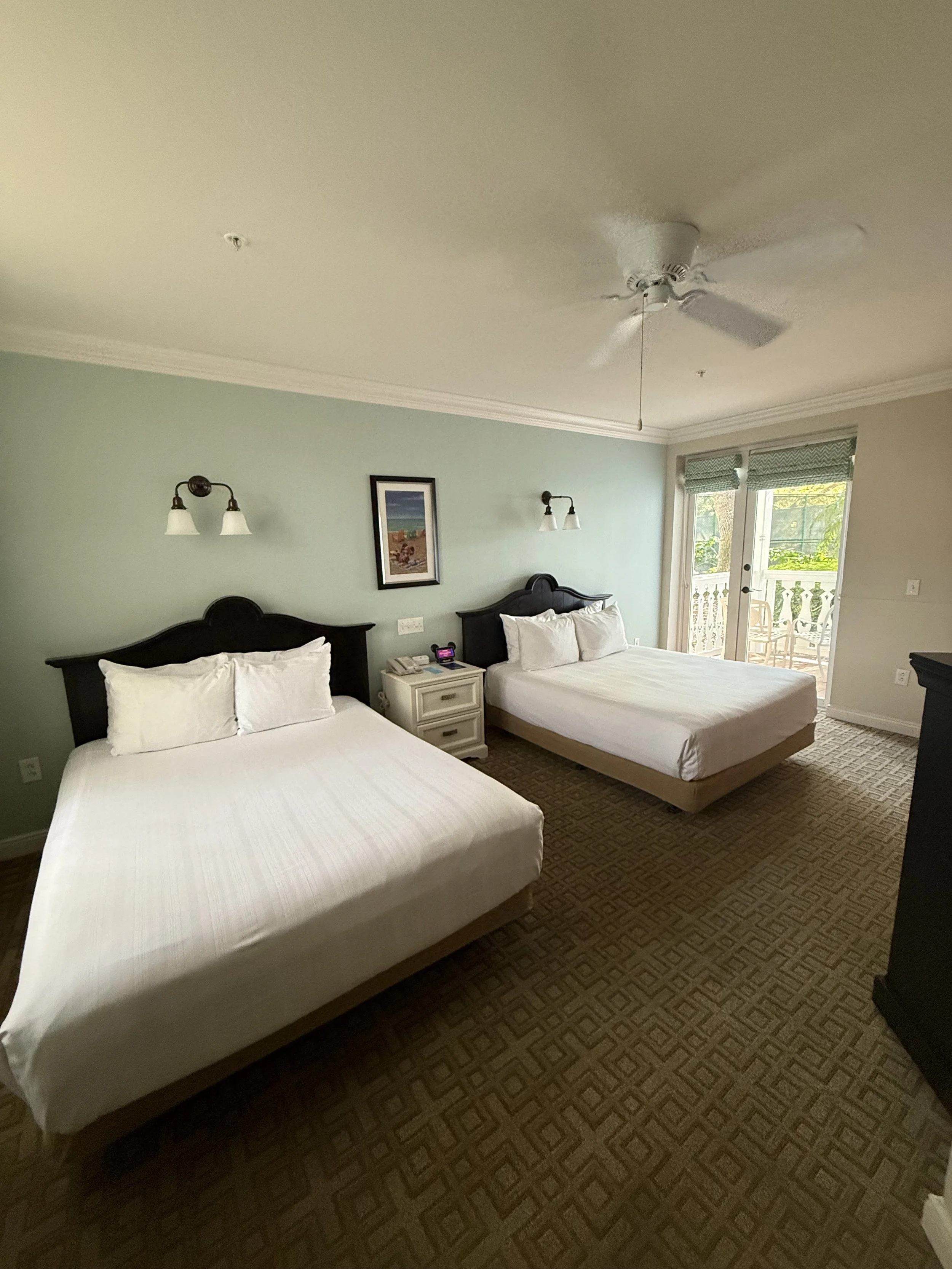 Hotel room with two queen beds, nightstand, and balcony access.