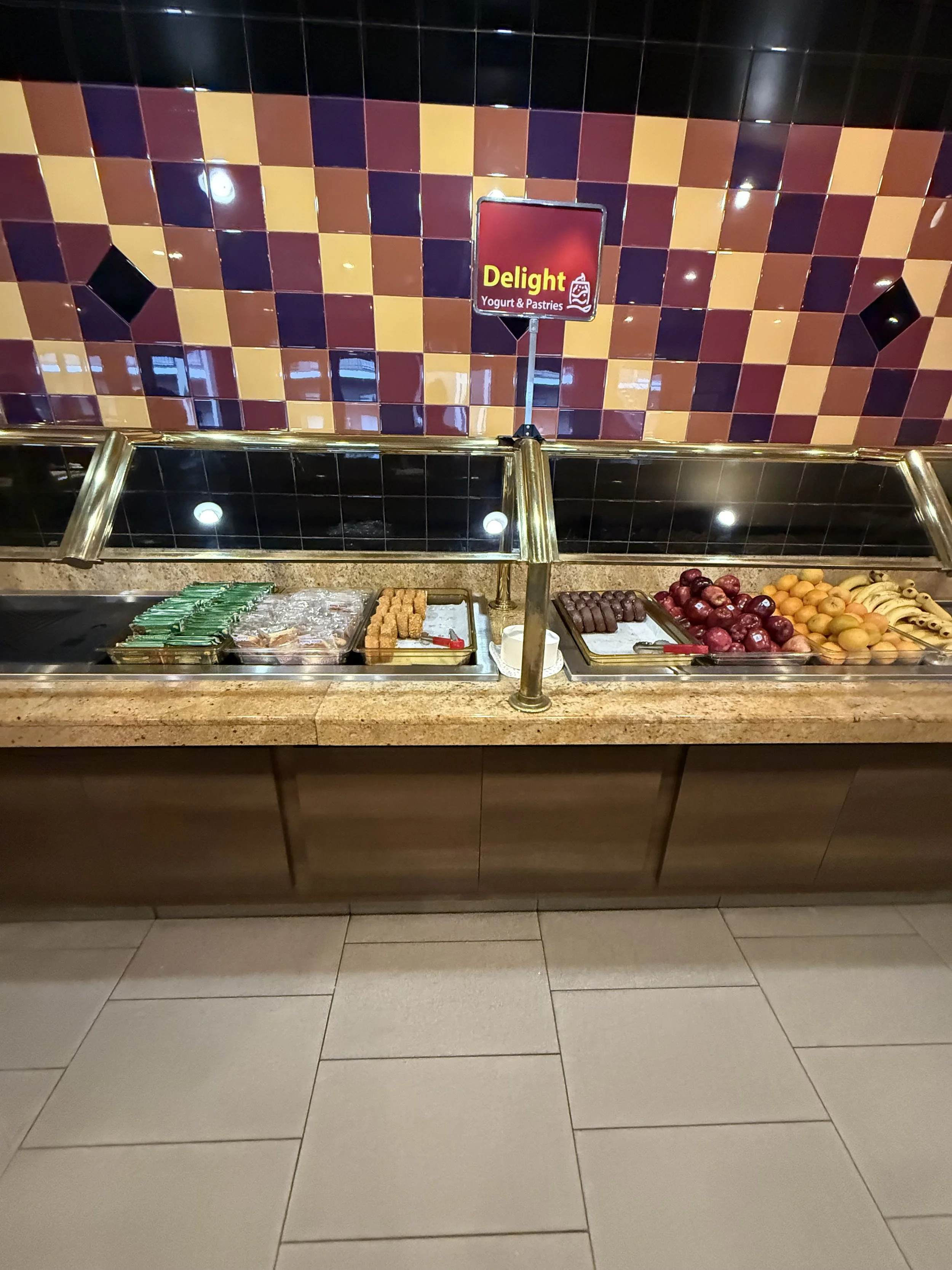 Buffet with assorted candies and fruits, including chocolate bars, gummy candies, strawberries, grapes, and bananas. Sign above reads 'Delight Yogurt & Pastries'.