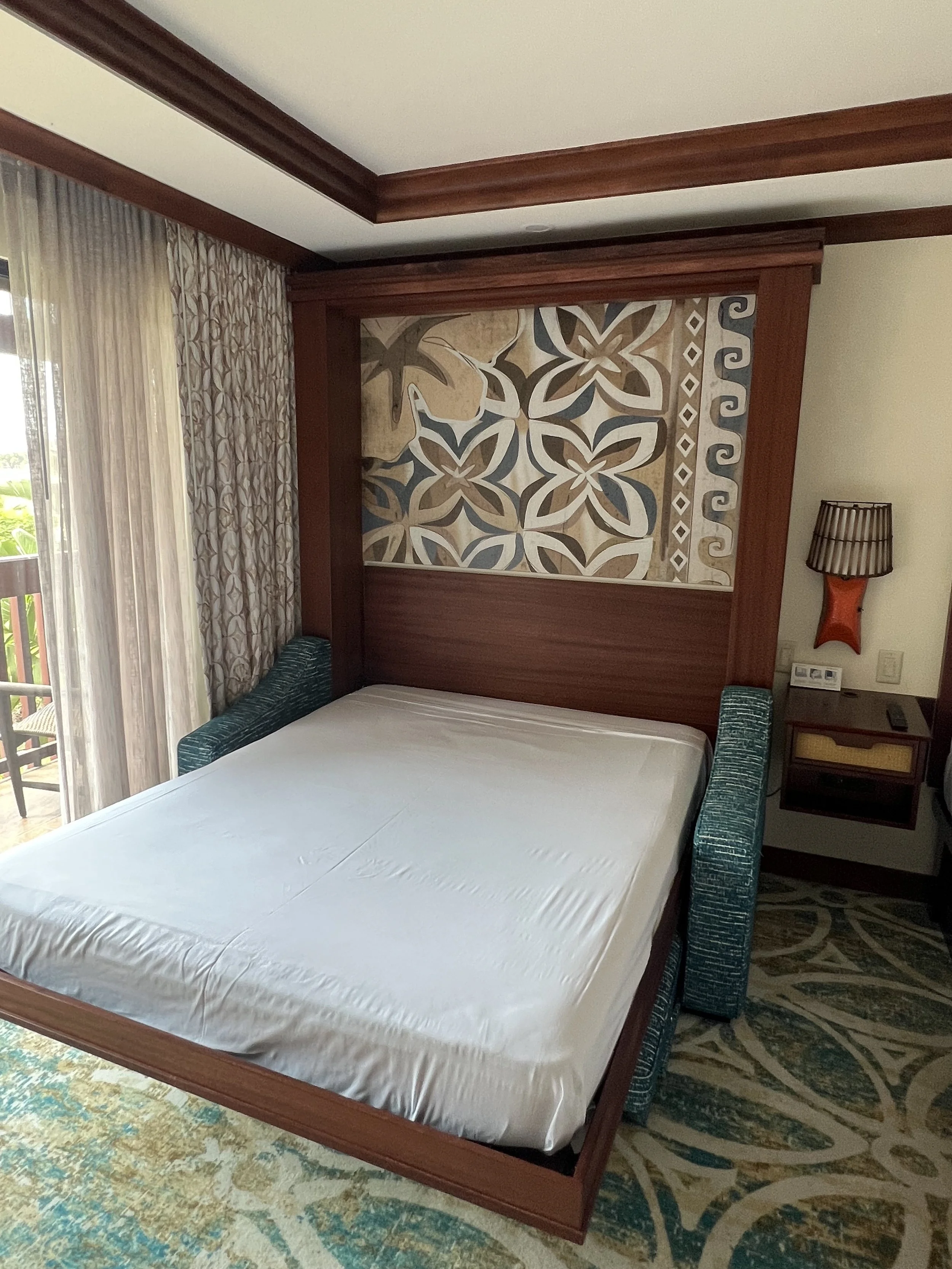 Hotel room with a bed, patterned headboard, curtains, and balcony door.