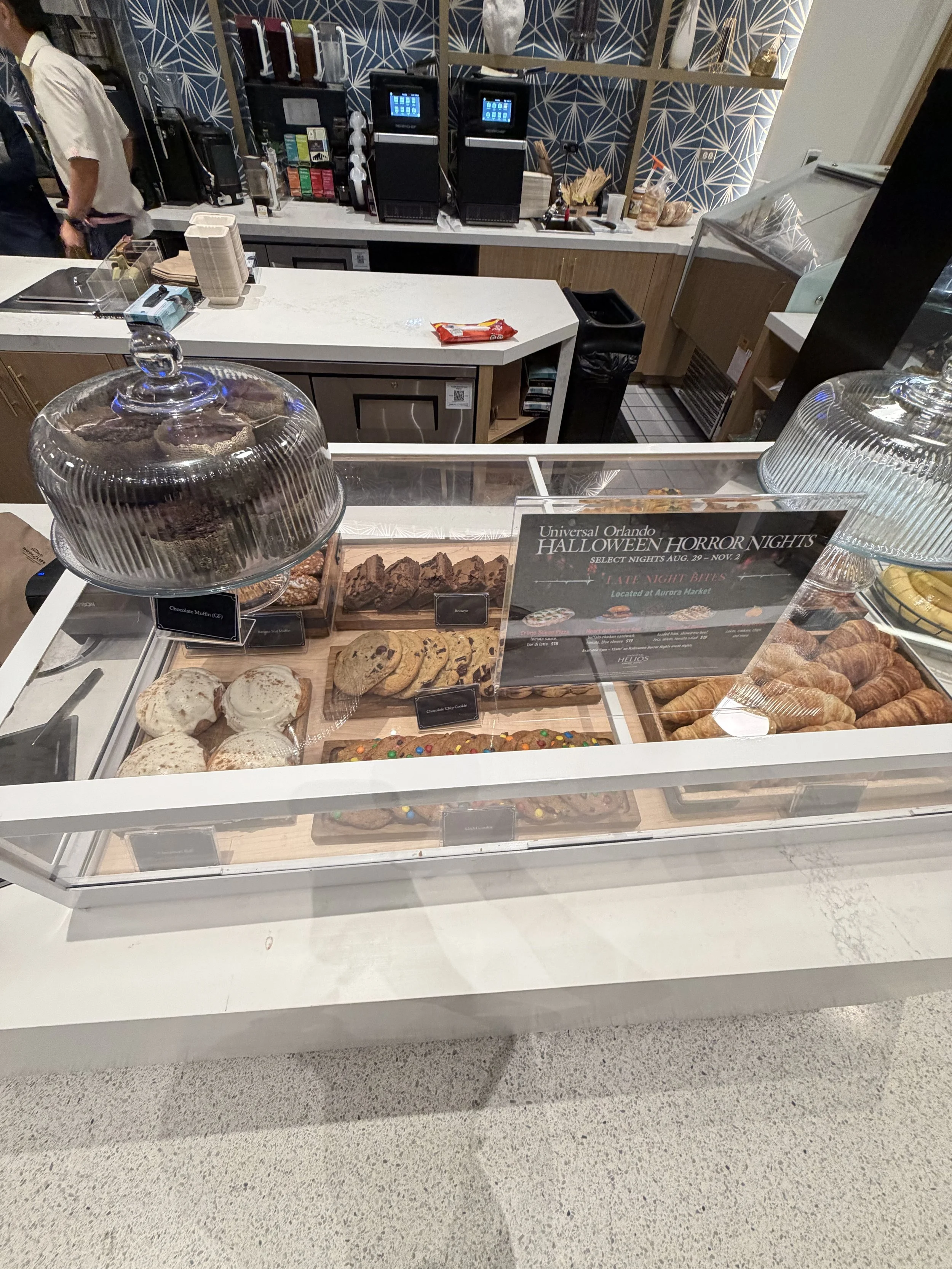 Display case with various baked goods including muffins, cookies, and croissants, with a sign for Halloween Horror Nights at Universal Orlando.