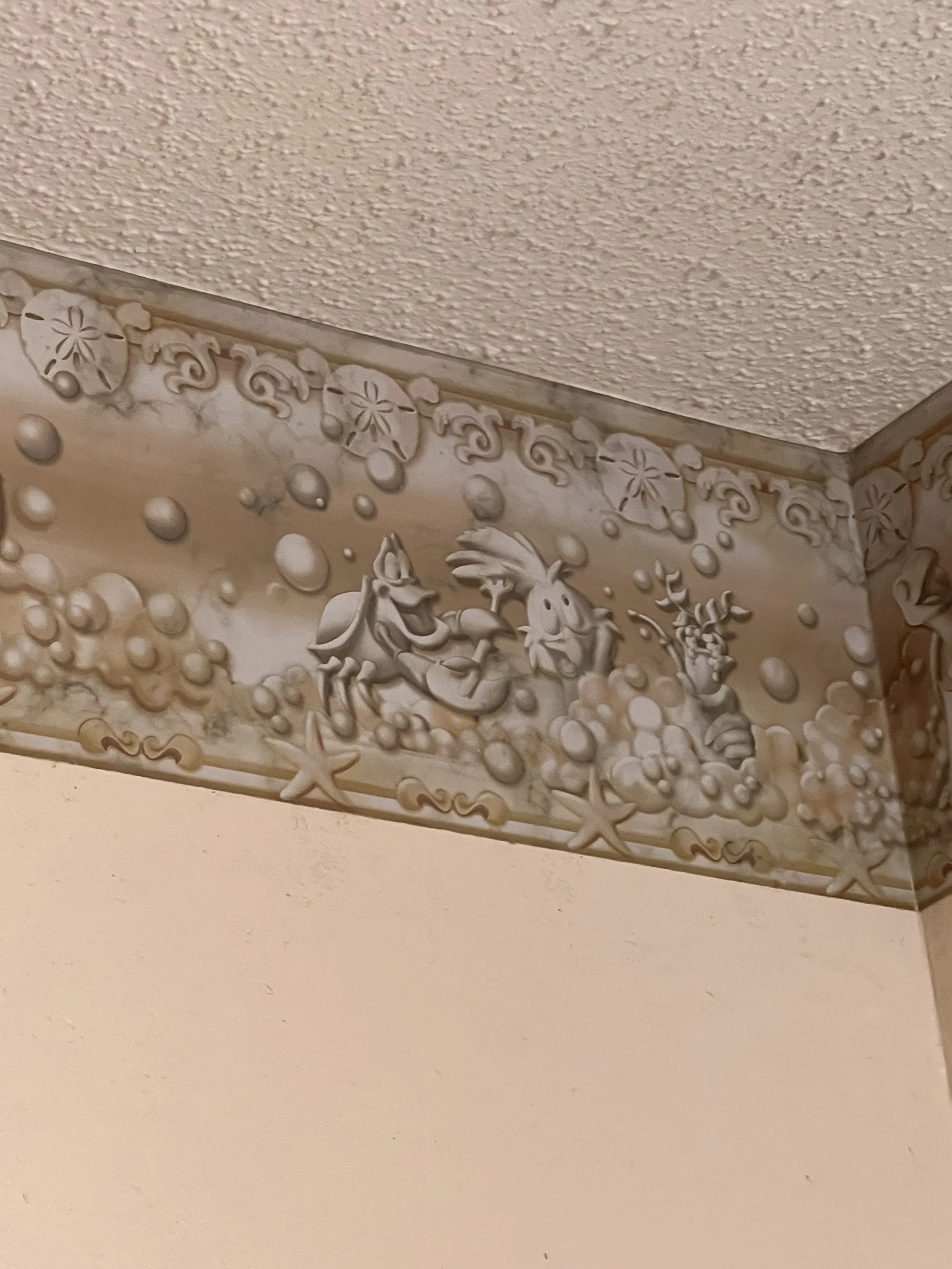 Decorative border near ceiling featuring Disney characters Pluto and Mickey Mouse surrounded by bubbles, starfish, and floral designs.