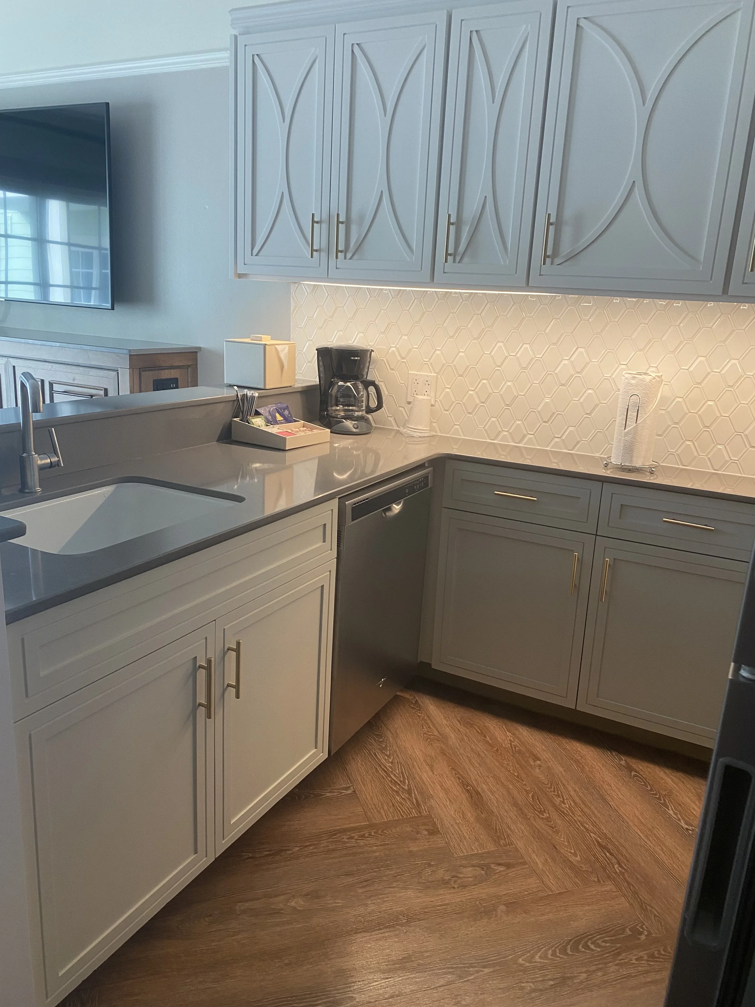 Kitchen with white cabinets, a gray countertop, a coffee maker, paper towels, and a tiled backsplash.