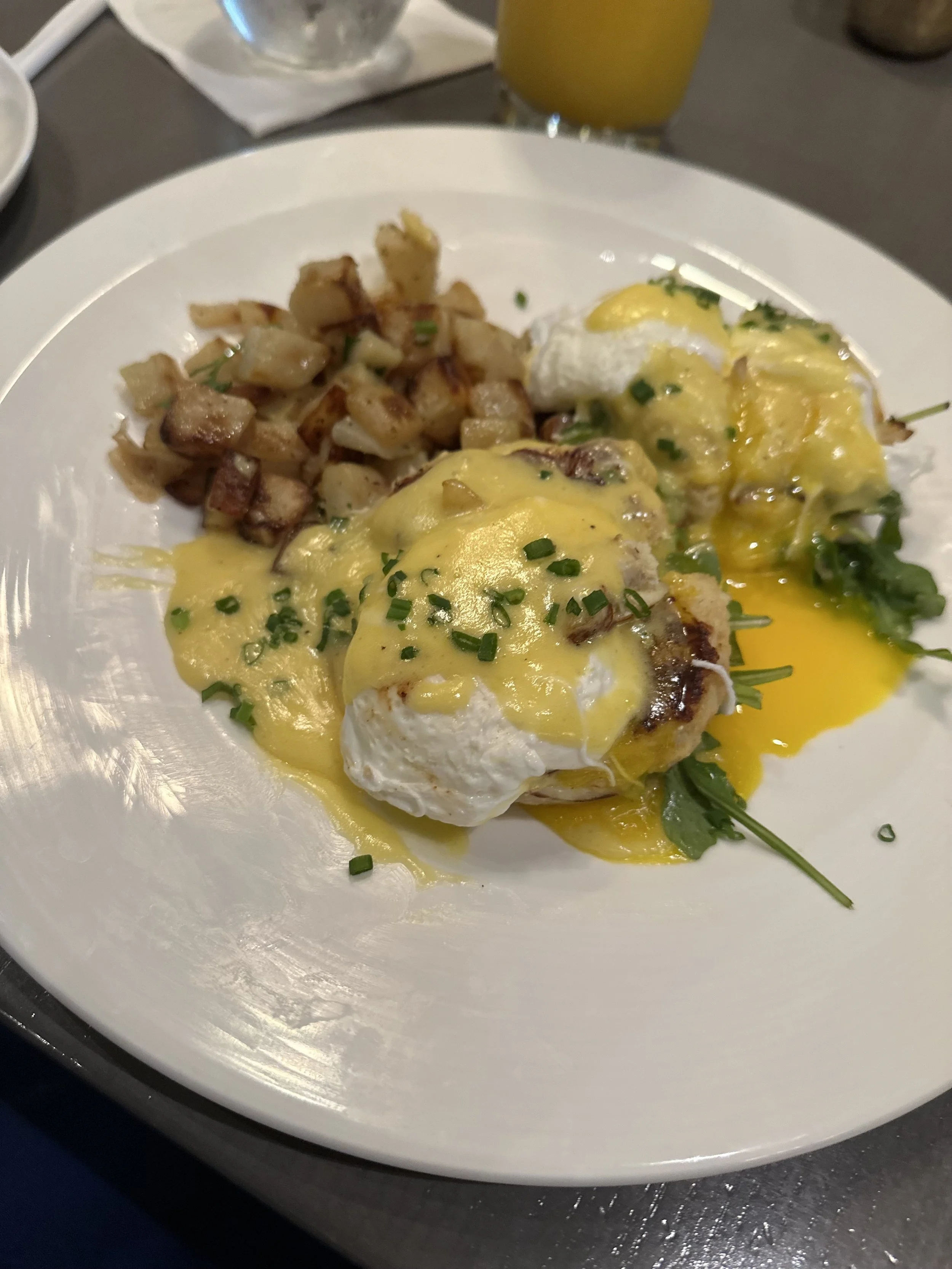 Eggs Benedict with hollandaise sauce, diced potatoes, and garnished with chopped chives on a white plate.