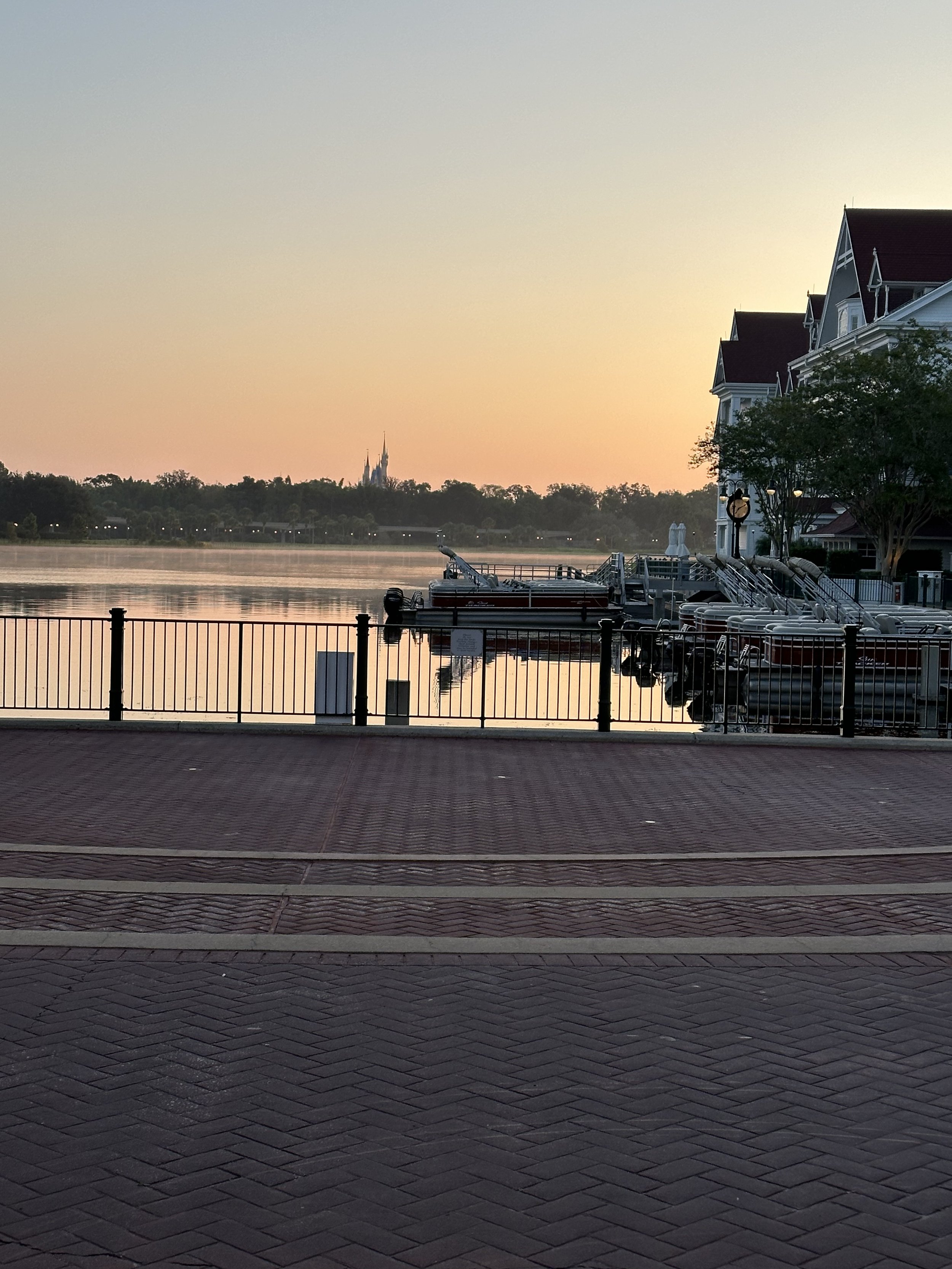 Sunrise over a calm river with docks and boats, residential buildings, and trees along the riverbank.