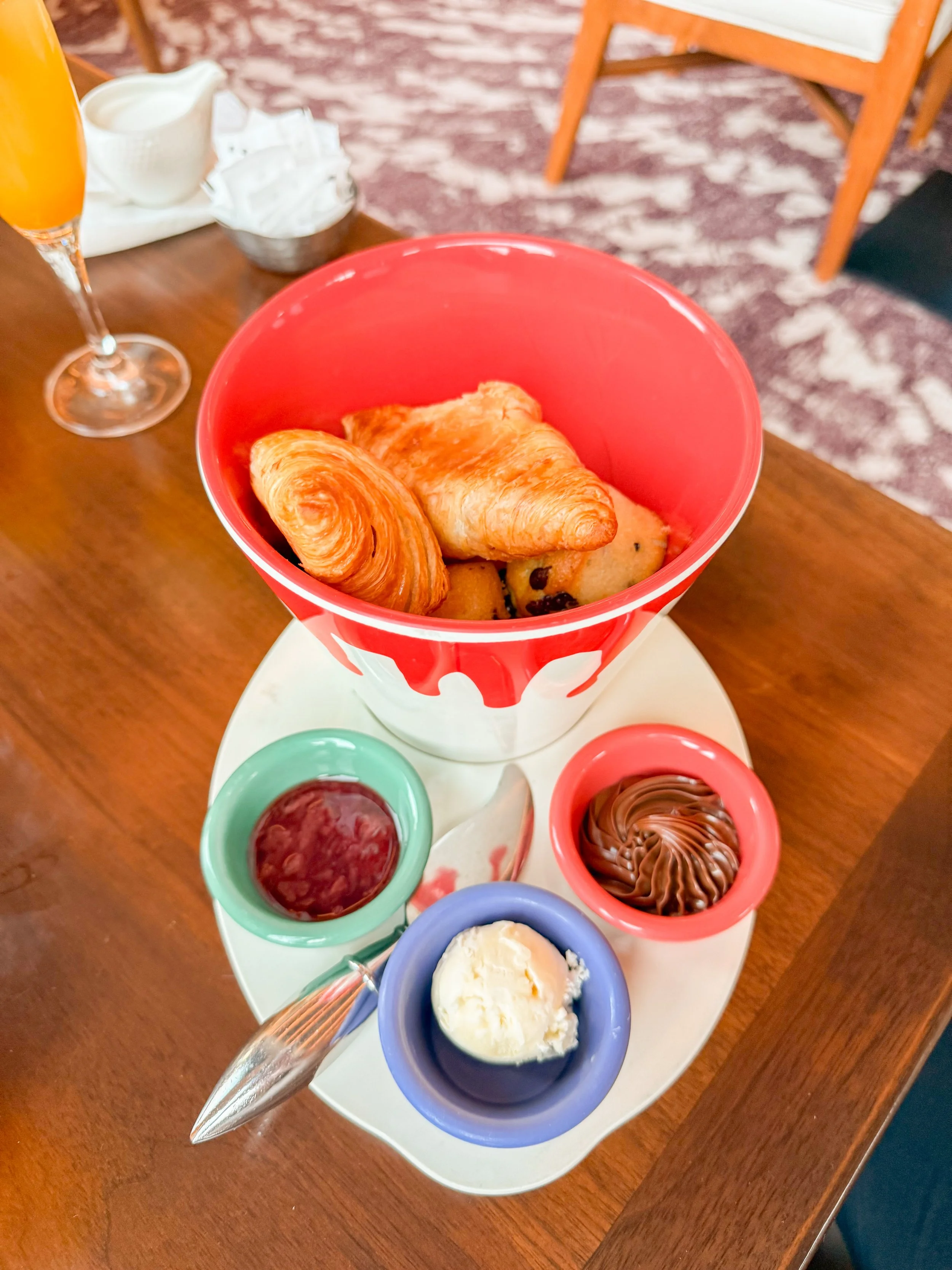 A serving of assorted breakfast pastries, including a croissant and a Danish pastry, with sides of jam, chocolate spread, and vanilla ice cream, on a white tray on a wooden table.