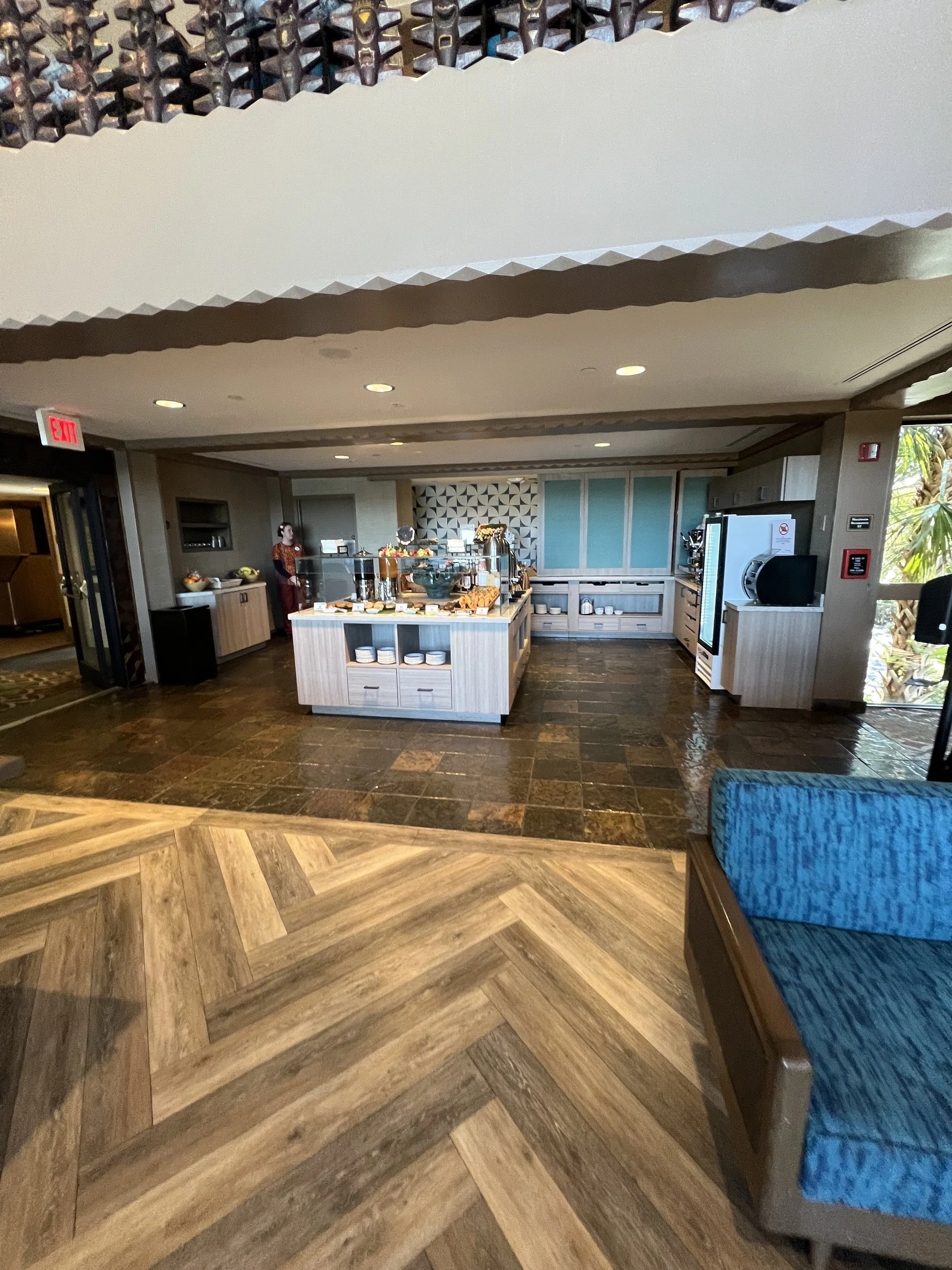 Buffet area with food and drink stations in a hotel or restaurant setting, with a woman standing near the serving area.