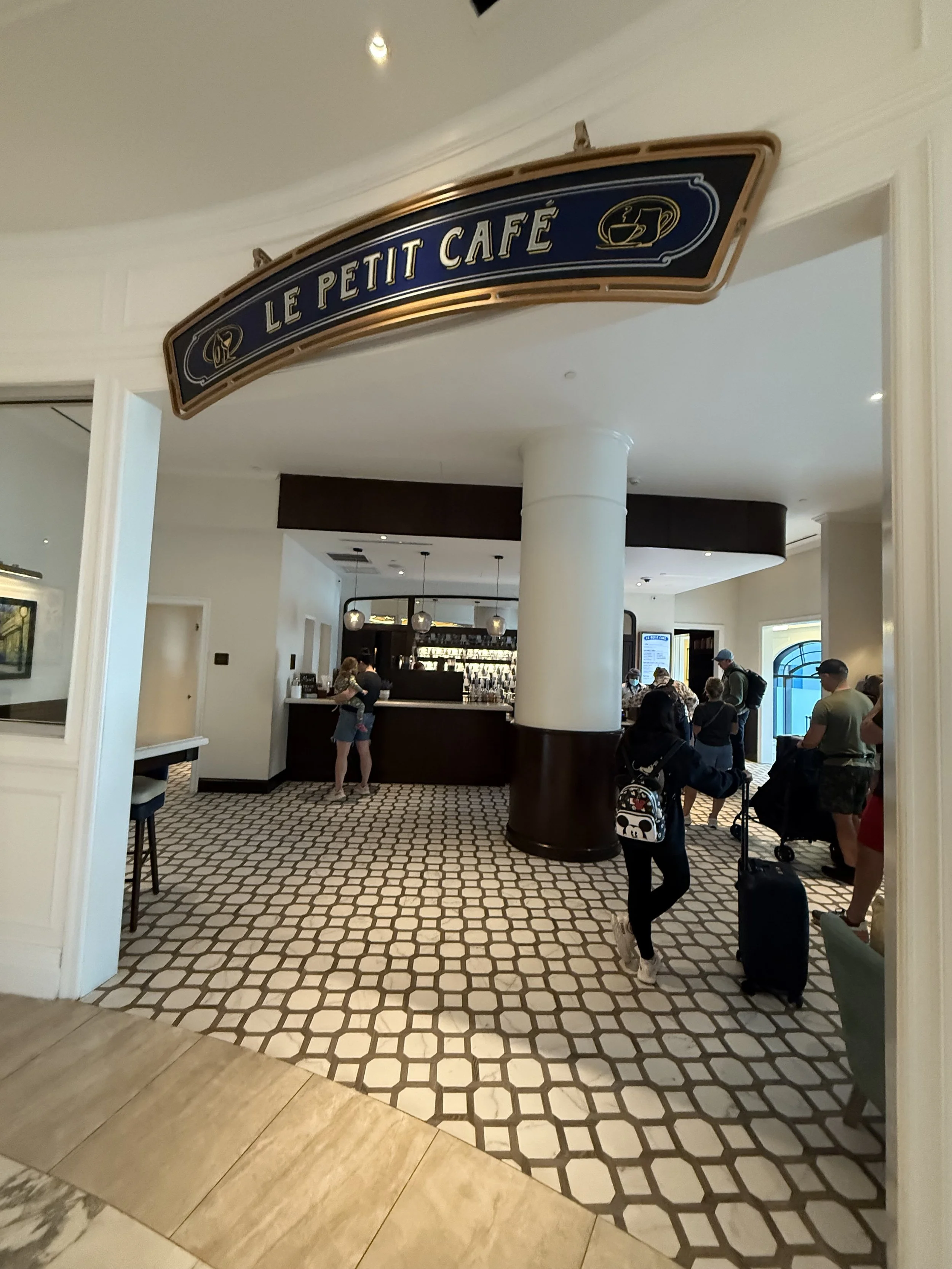Entrance to Le Petit Cafe with people standing in line and luggage.