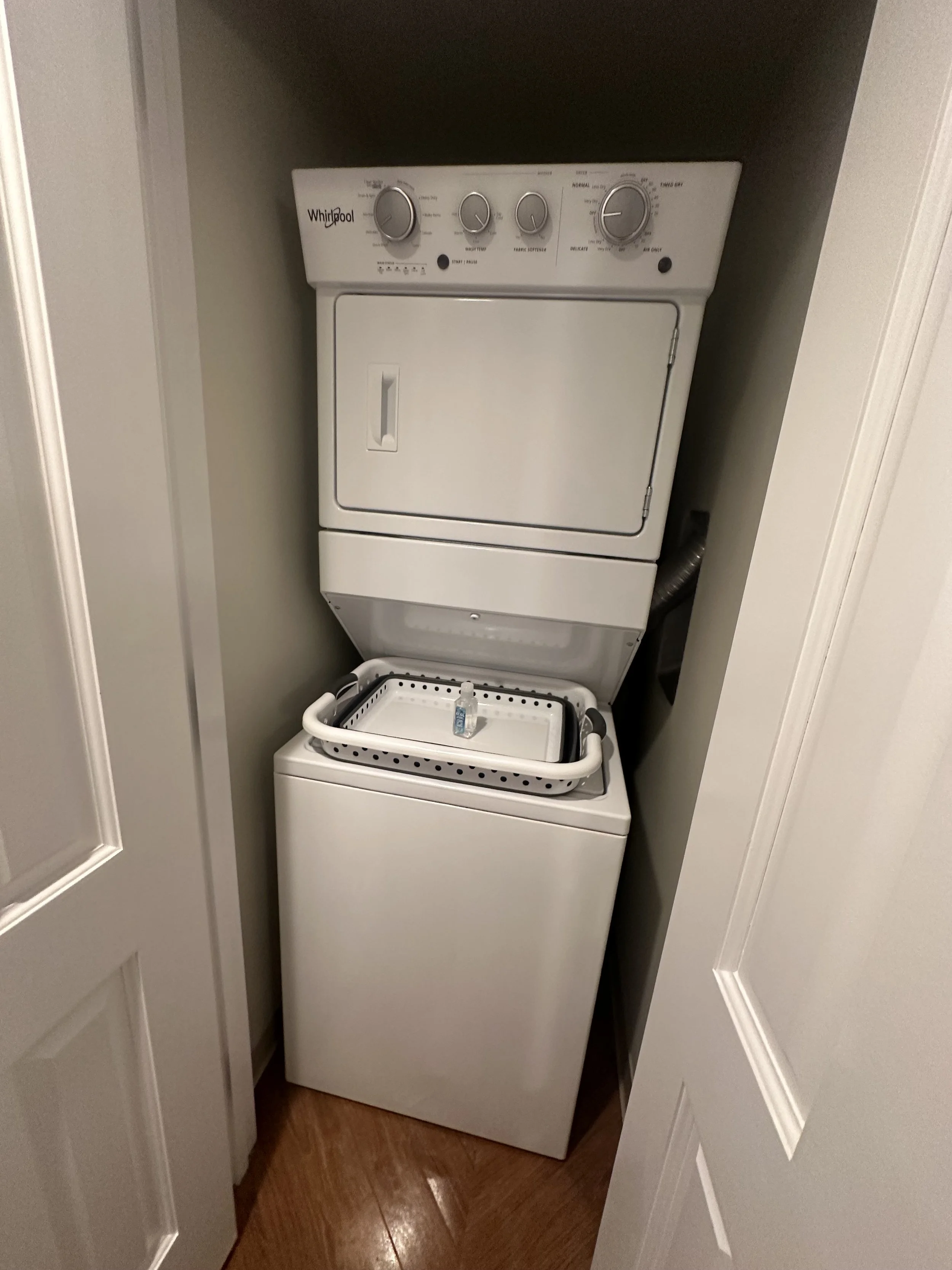 A stacked washer and dryer in a small laundry closet, with a laundry basket on top.