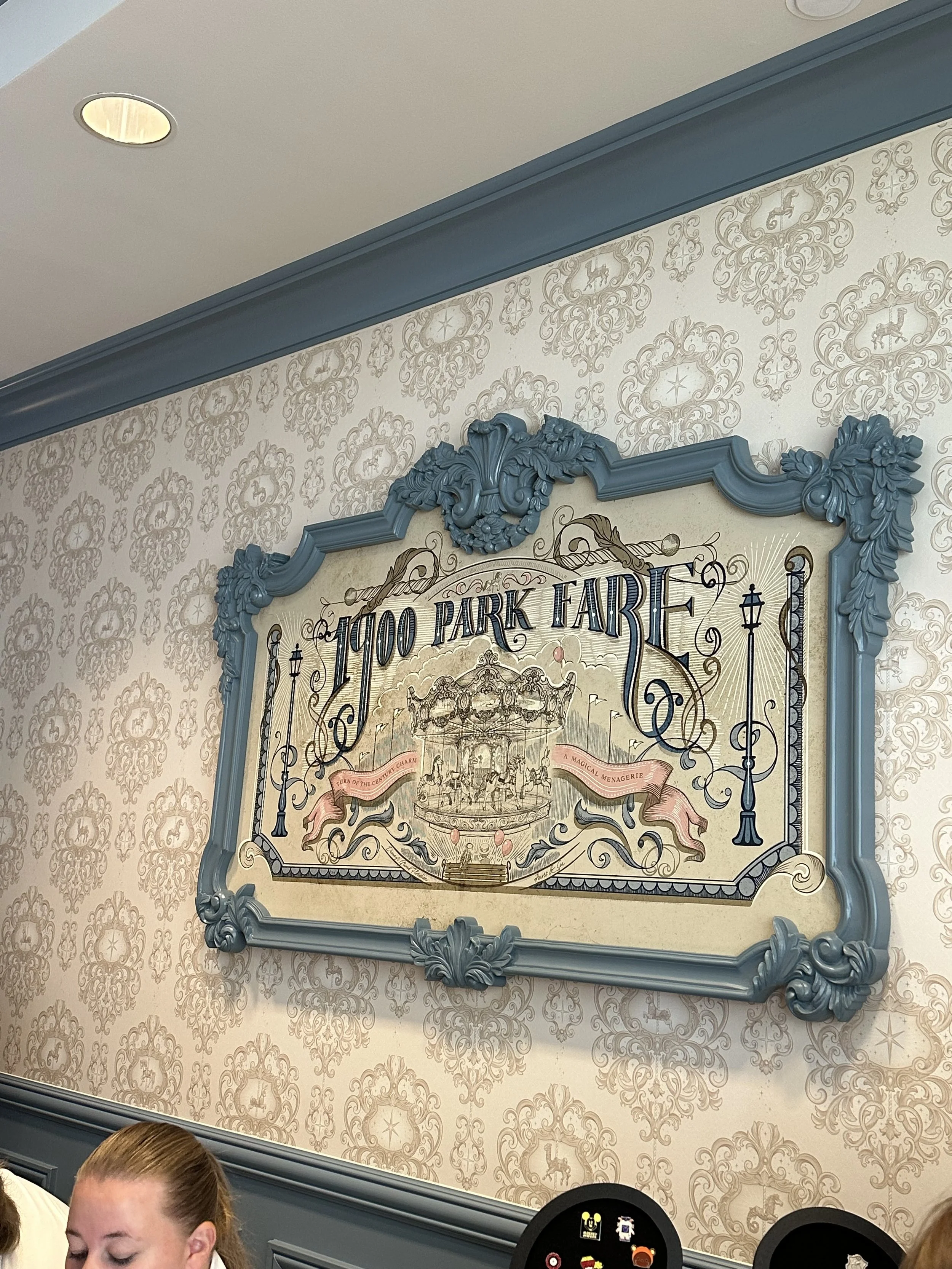 Decorative sign for H700 Park Fare, a restaurant at Disney's Grand Floridian Resort & Spa, featuring a vintage carousel illustration and ornate blue frame.